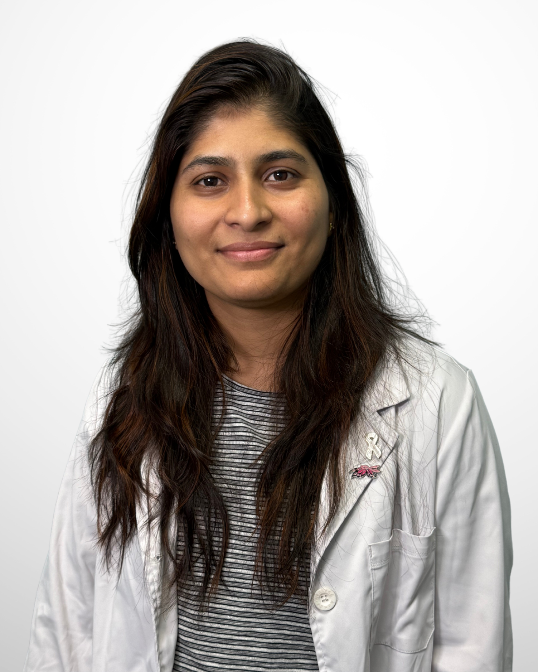 A woman with long dark hair wearing a white lab coat and a striped shirt, smiling at the camera, with a neutral background.