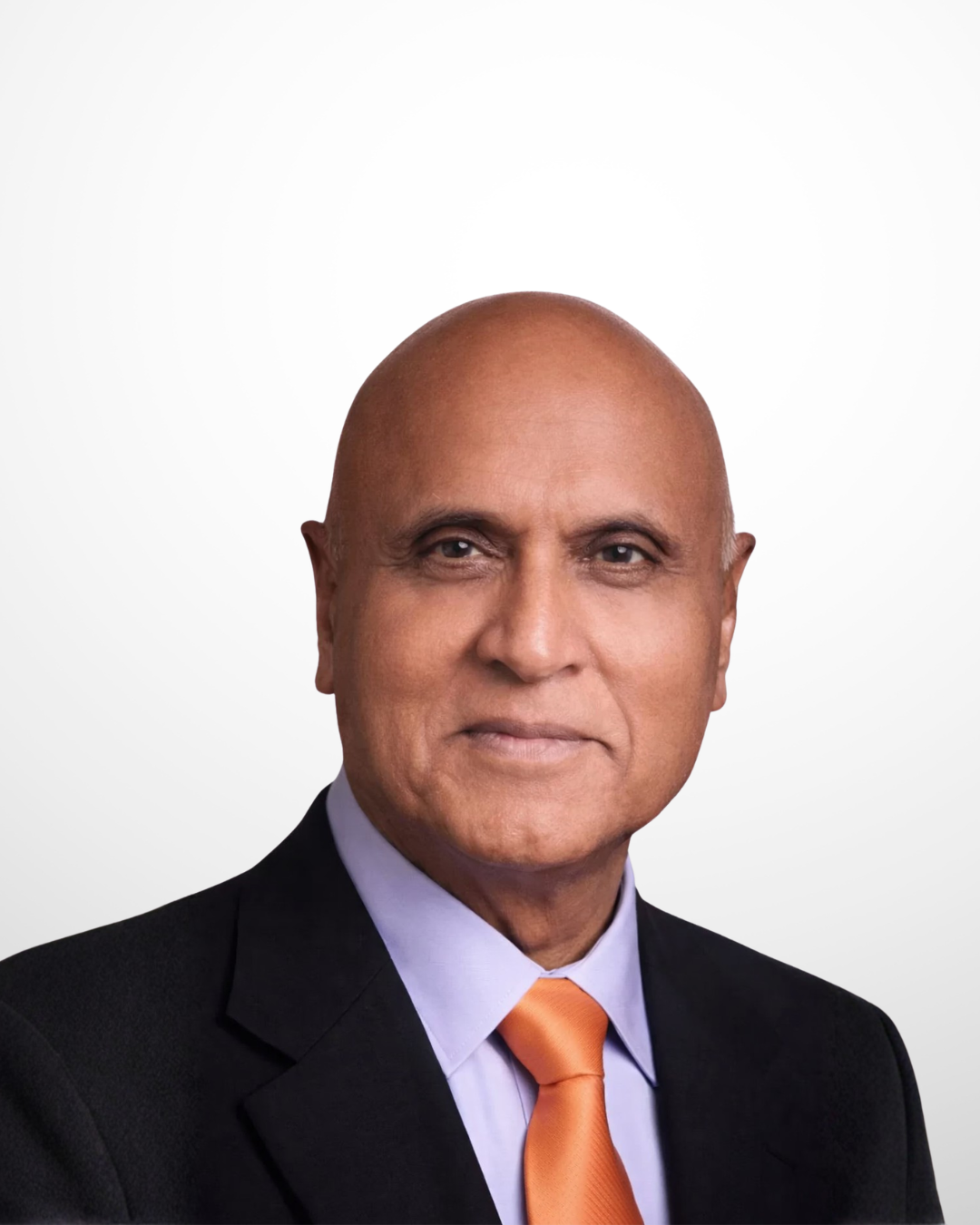 A smiling male doctor in a black suit, wearing a shirt and tie, against a plain white background.