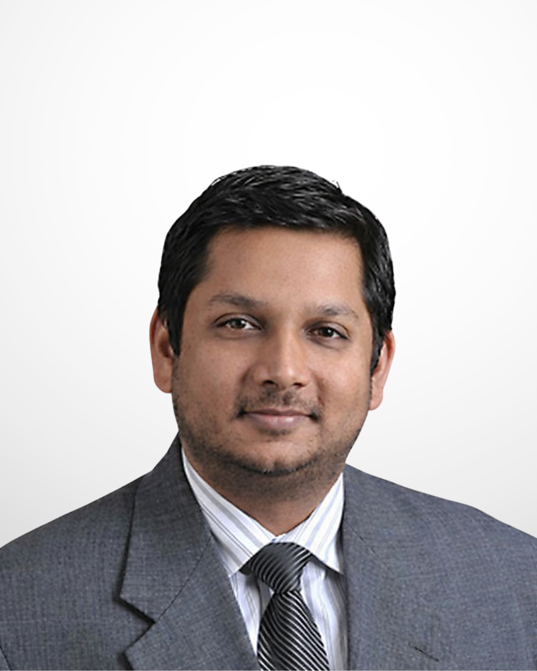 A smiling male doctor in a grey suit, wearing a shirt and tie, against a plain white background.