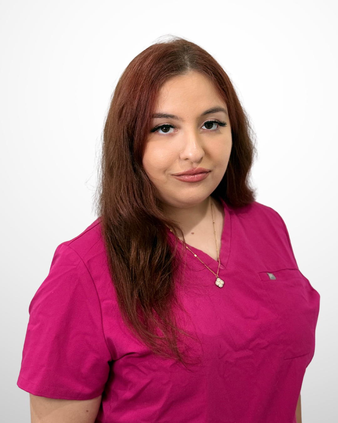 A woman with long red hair wearing a pink medical scrub top, standing against a plain white background.