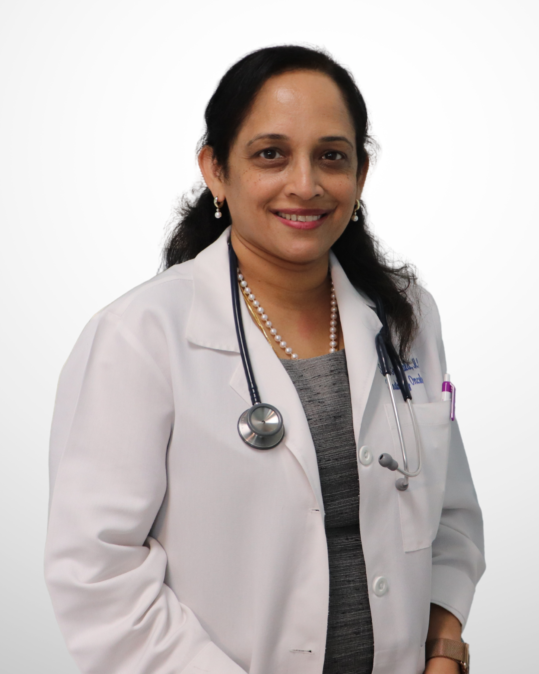 A smiling female doctor with dark hair, dressed in a white coat with a stethoscope around her neck, standing against a plain white background.
