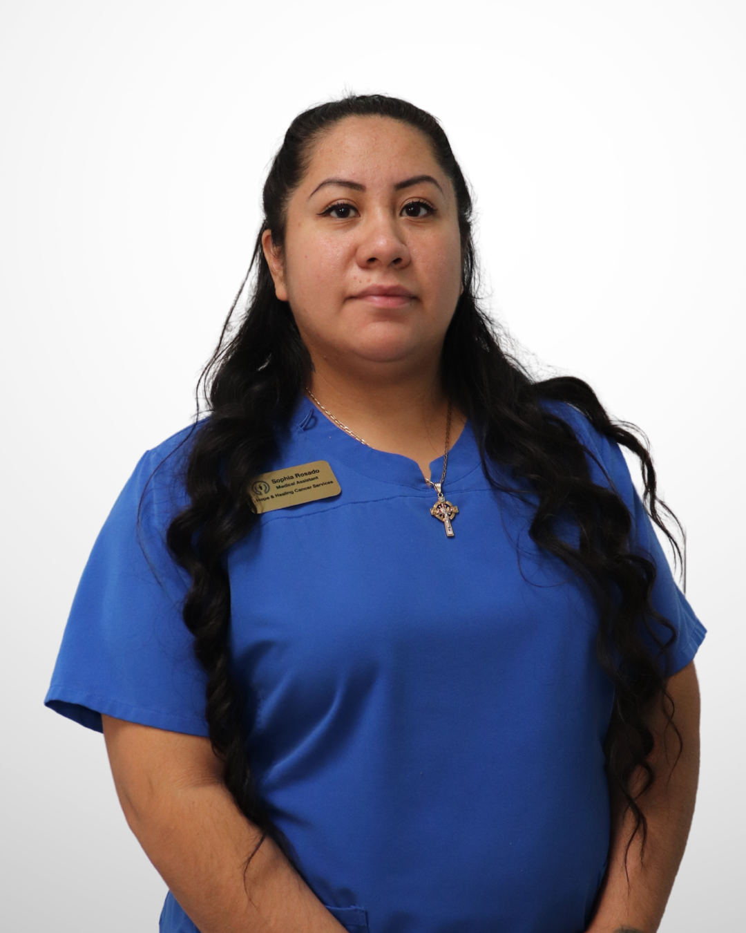 A woman in blue scrubs with a name tag reading 'Sophia Rosado' and a cross necklace standing against a white background.