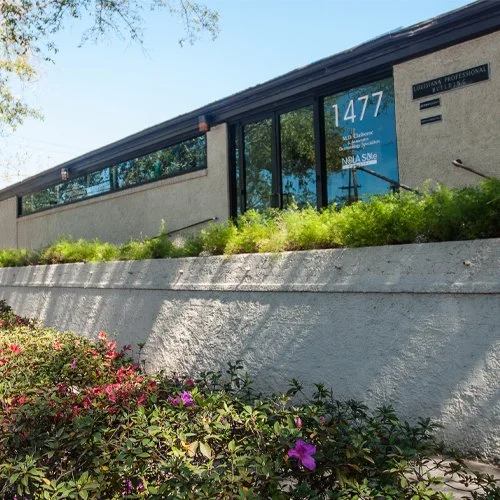 Exterior of a building with large glass windows, a blue address sign that reads '1477', and a small sign indicating it is a professional office.