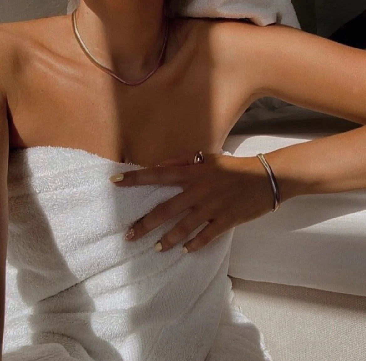 Female upper torso with nice spray tan, wrapped in white towel with left hand wearing thumb ring and bracelet and a necklace around neck.