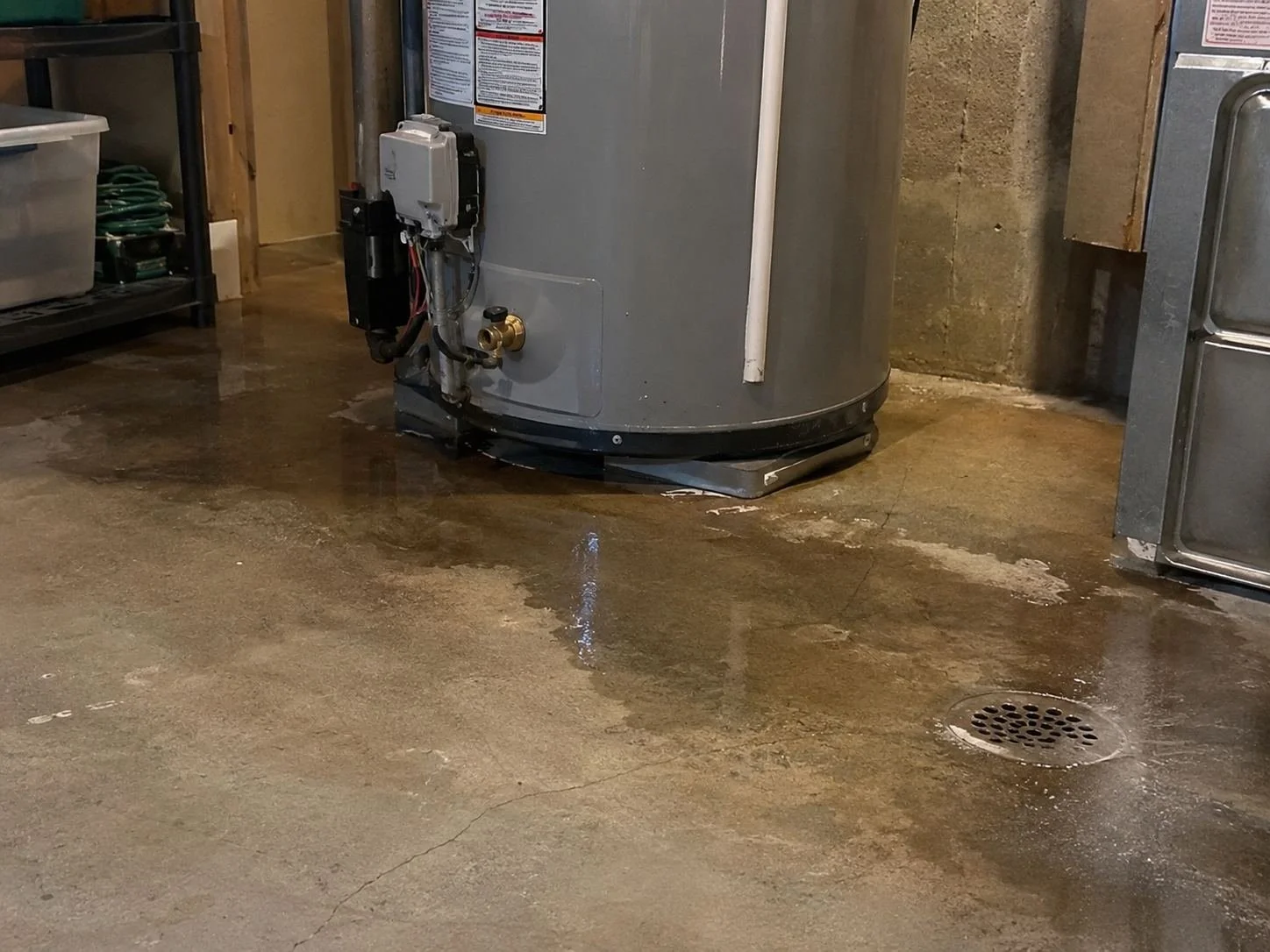 Leaking water heater with a shallow puddle in a Lenexa, KS utility room