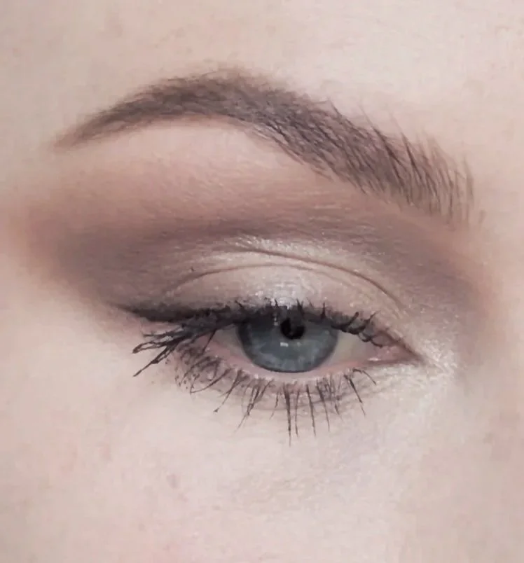 Close-up of a person's eye with makeup, showing a blue iris, long eyelashes, and defined eyebrow.