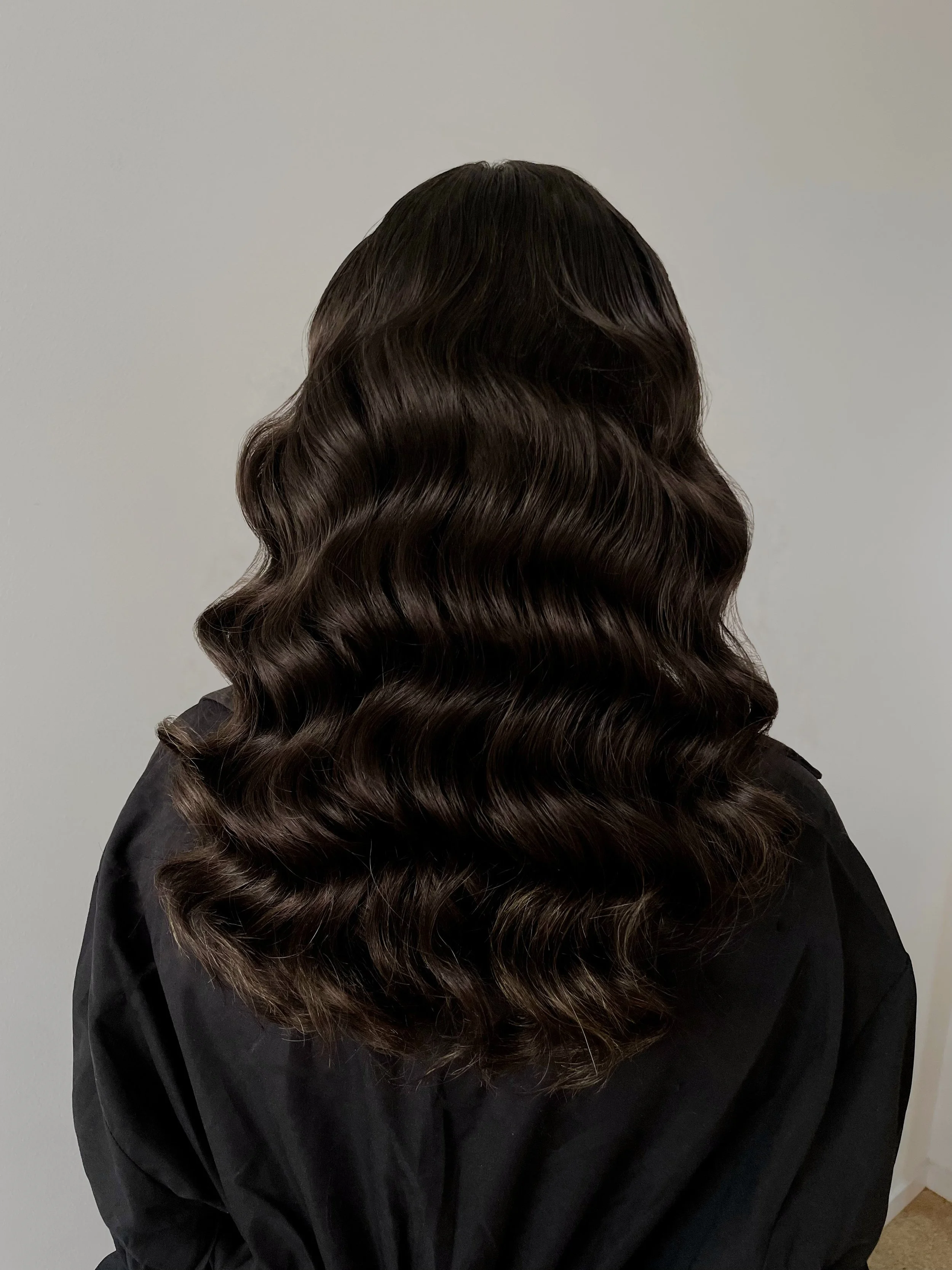 Back view of a woman with long, wavy, dark brown hair wearing a black top.