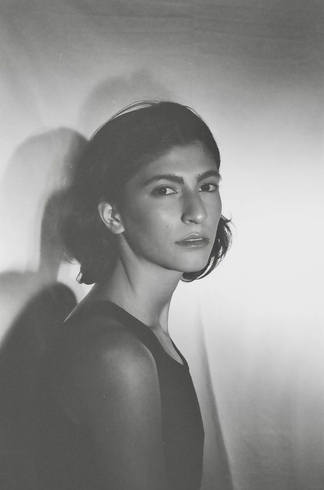 Black and white portrait of a woman with short wavy hair, wearing a sleeveless top, looking at the camera with a calm expression, against a plain background.