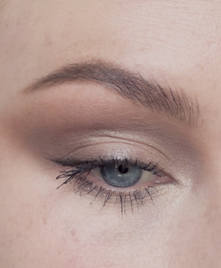 Close-up of a woman's eye with neutral eyeshadow, eyeliner, and mascara, showing well-groomed eyebrows and long eyelashes.