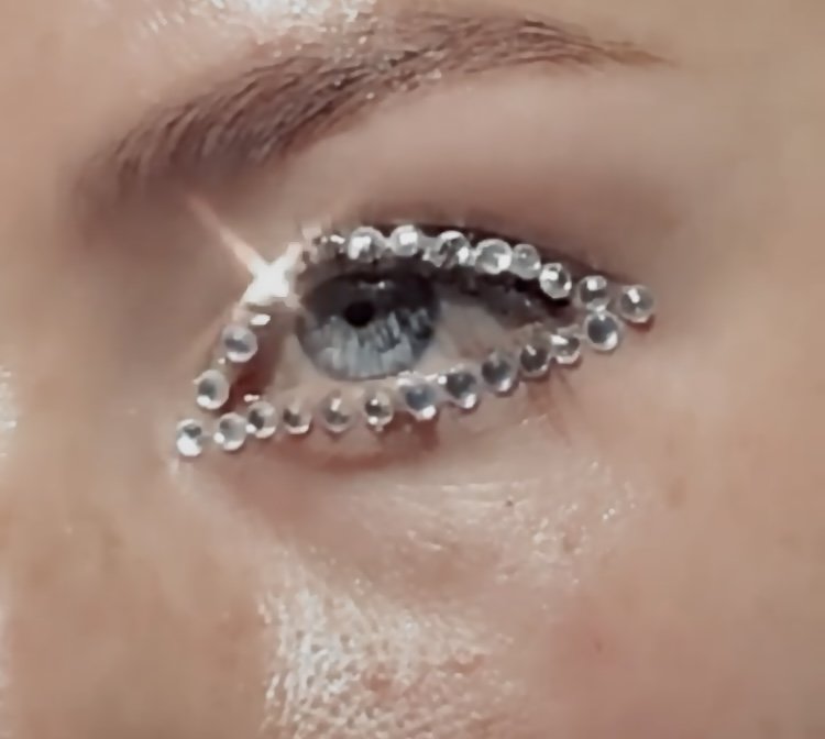 Close-up of a person's eye with a decorative rhinestone eye makeup design and makeup applied around the eye.