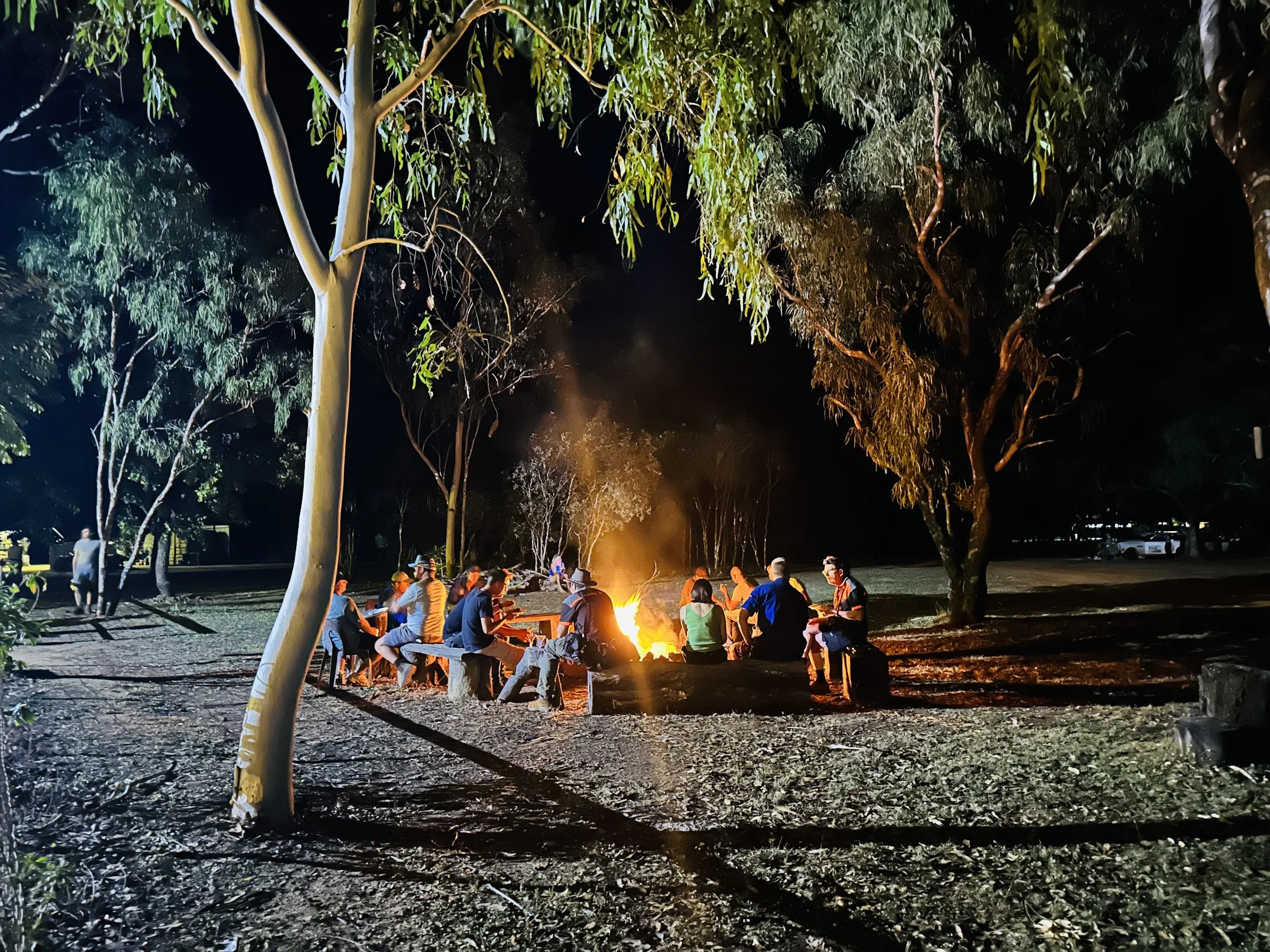 Group of people sitting around a campfire at night in a wooded area.