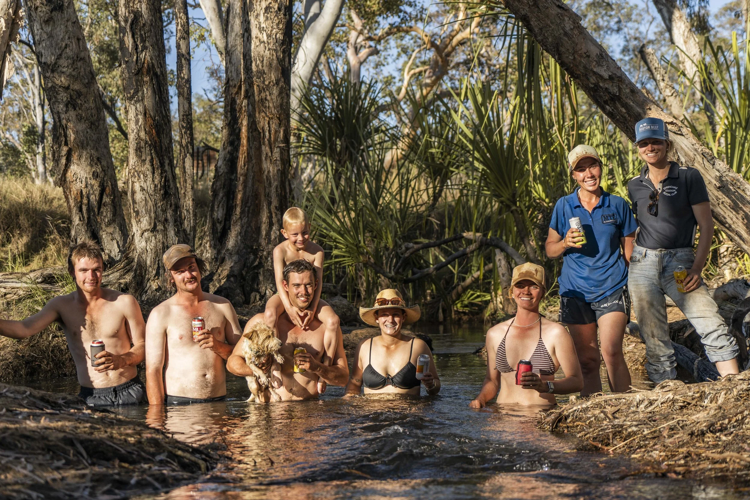 Group of people enjoying a swim and socializing in a creek surrounded by trees and greenery