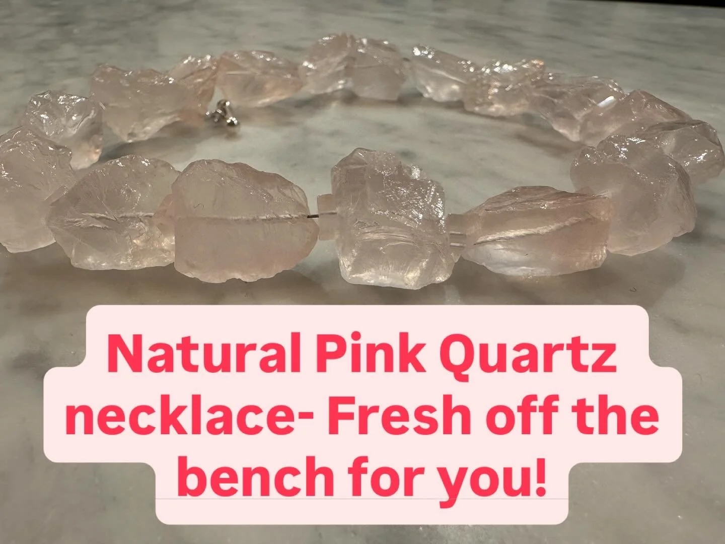 A natural pink quartz necklace made of irregularly shaped quartz stones laid out in a circle on a marble surface with text overlaid that says 'Natural Pink Quartz necklace- Fresh off the bench for you!'