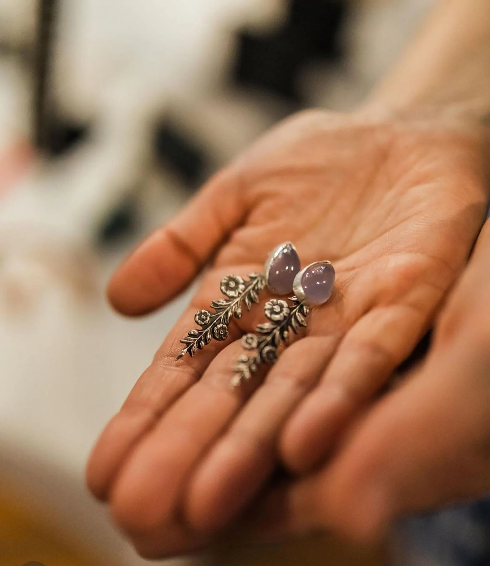 Close-up of a person's hand holding a pair of decorative earrings with purple stones and floral silver design.