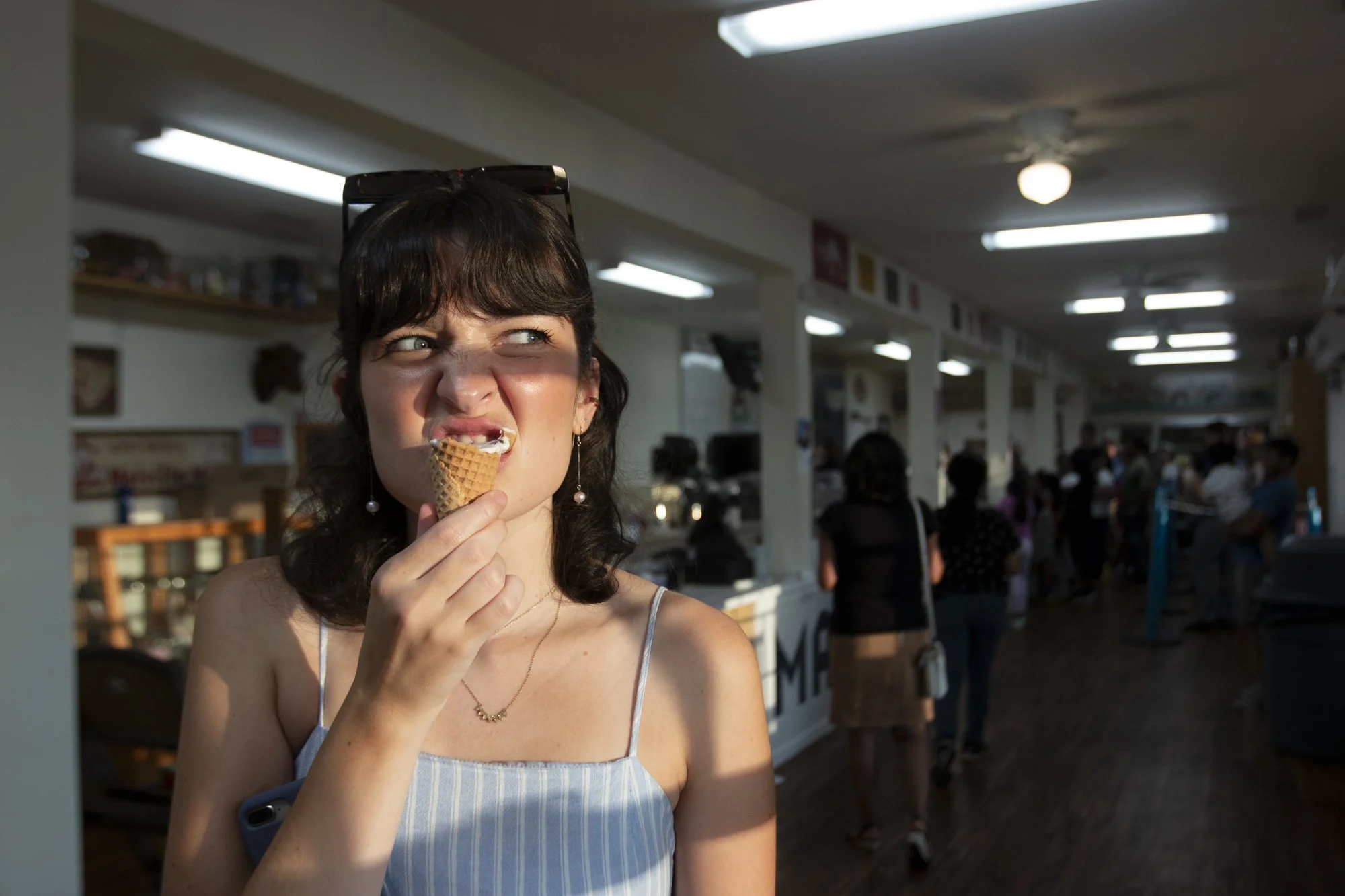 Young woman eating ice cream cone at Mapleview Ice Cream in NC with people in line in the background.