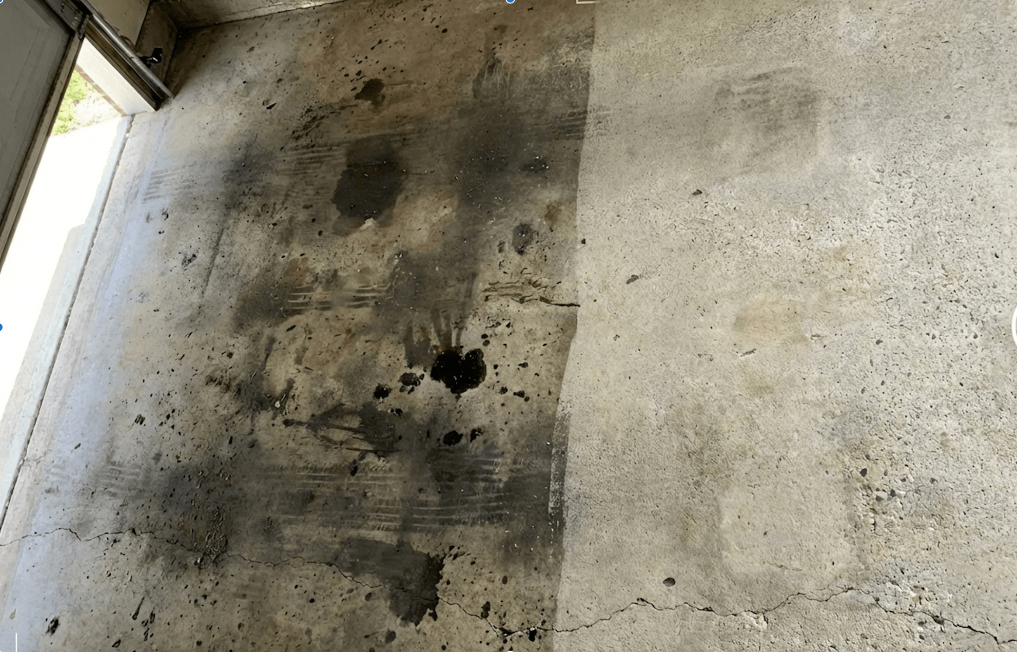 Concrete garage floor with dark oil stains, dirt, and cracks near the bottom.