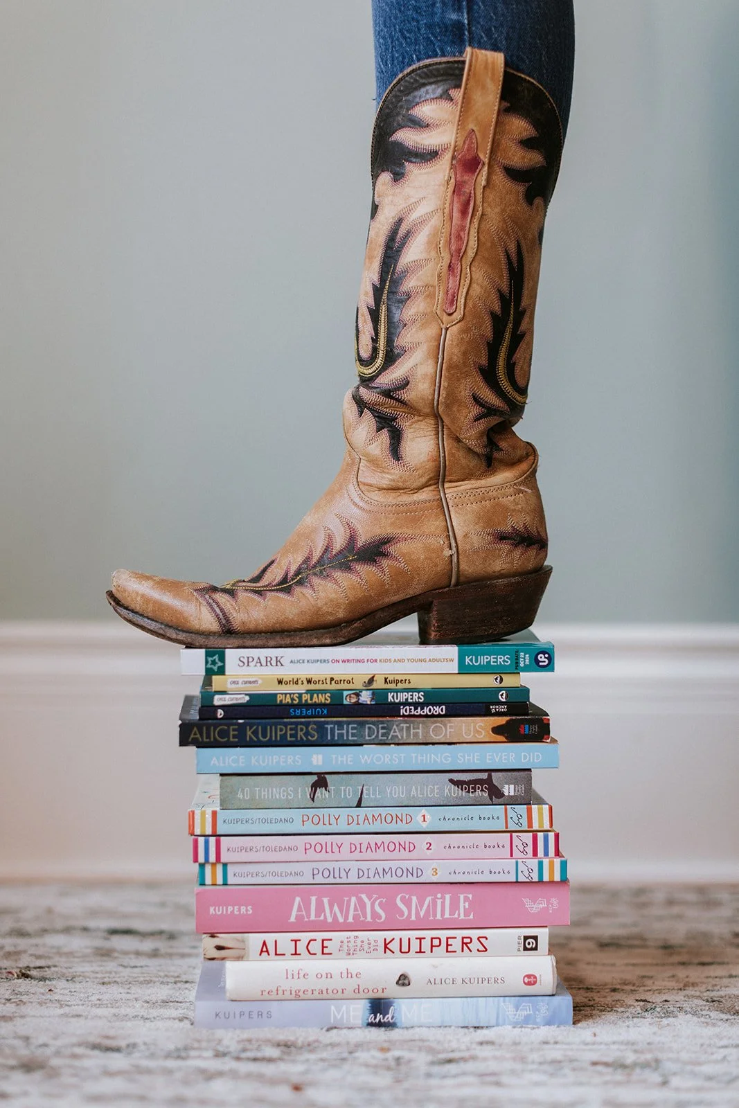 Alice Kuipers author stepping on a stack of her books with cowboy boot