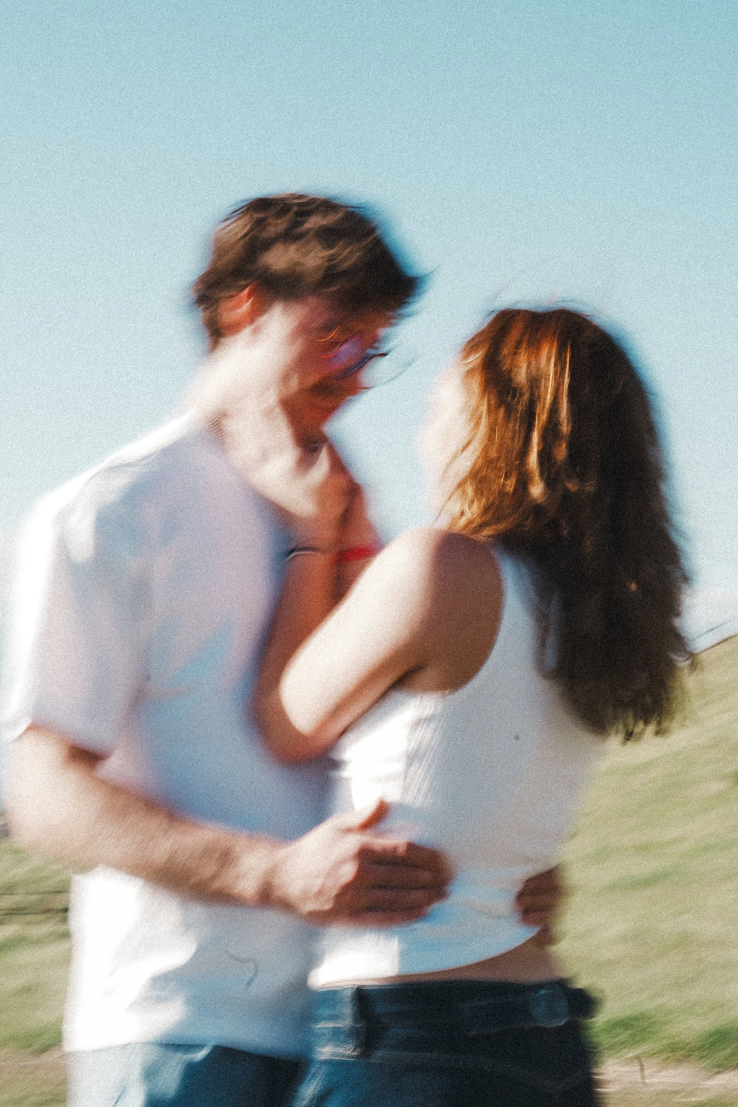 A blurry photo of a couple outdoors, looking at each other affectionately with a clear blue sky in the background.