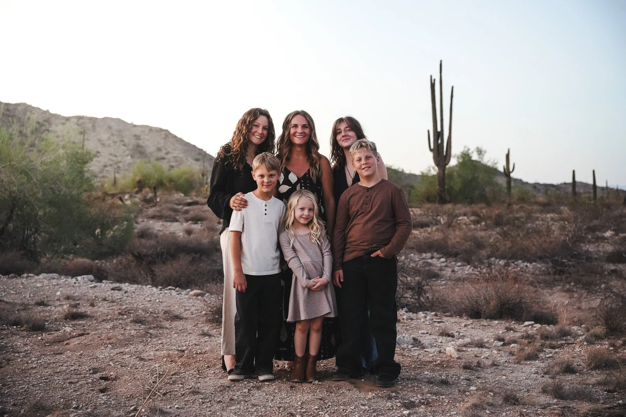 Family then standing together in desert landscape during dusk with cacti and mountains in background.