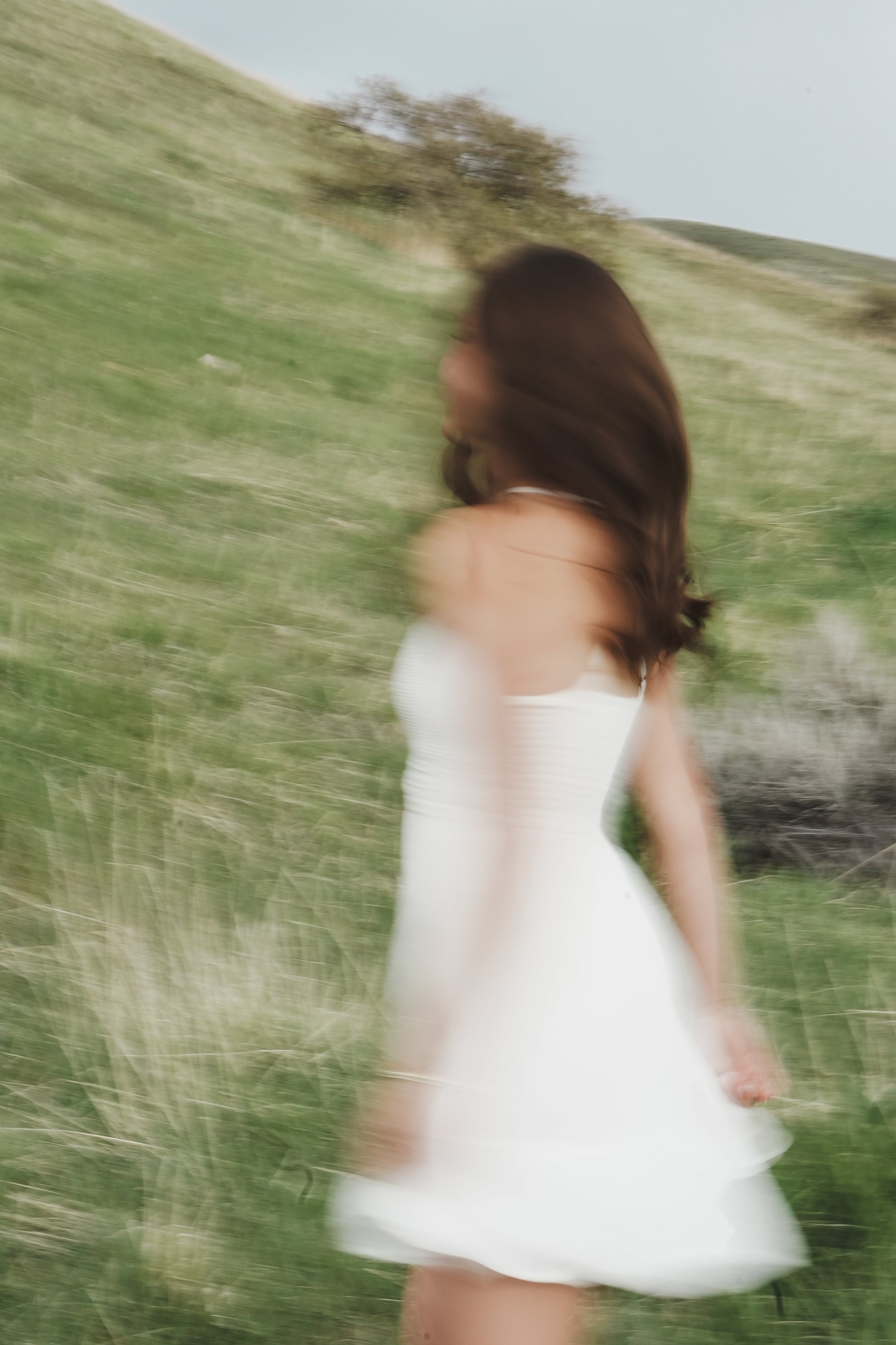Blurry photo of a woman in a white dress walking through grassy hills.