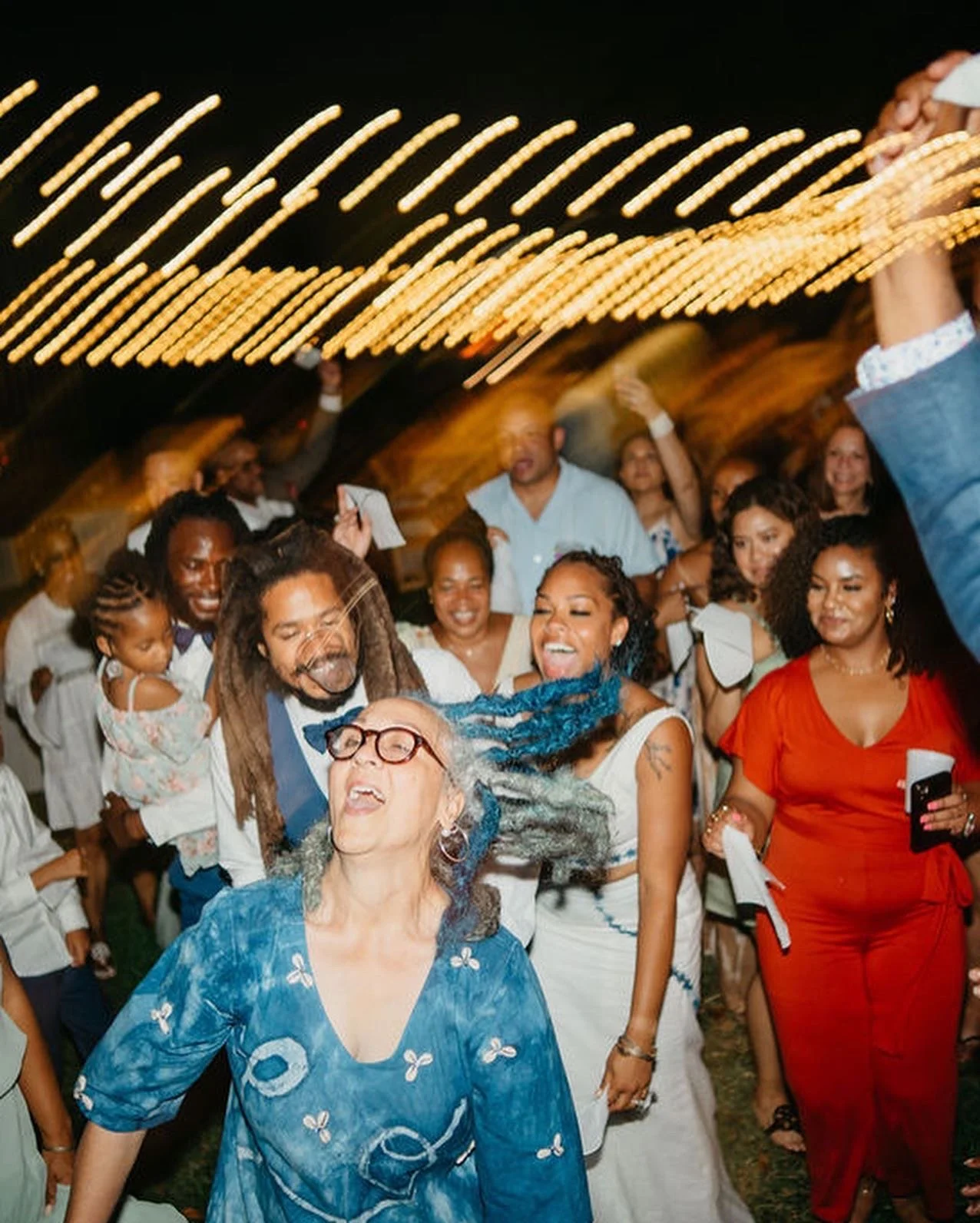 People dancing and celebrating at a lively party, with string lights overhead.
