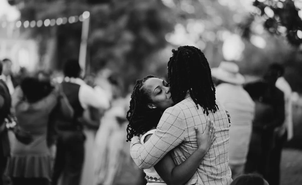 A couple dancing closely and embracing in a festive outdoor gathering, with others in the background.
