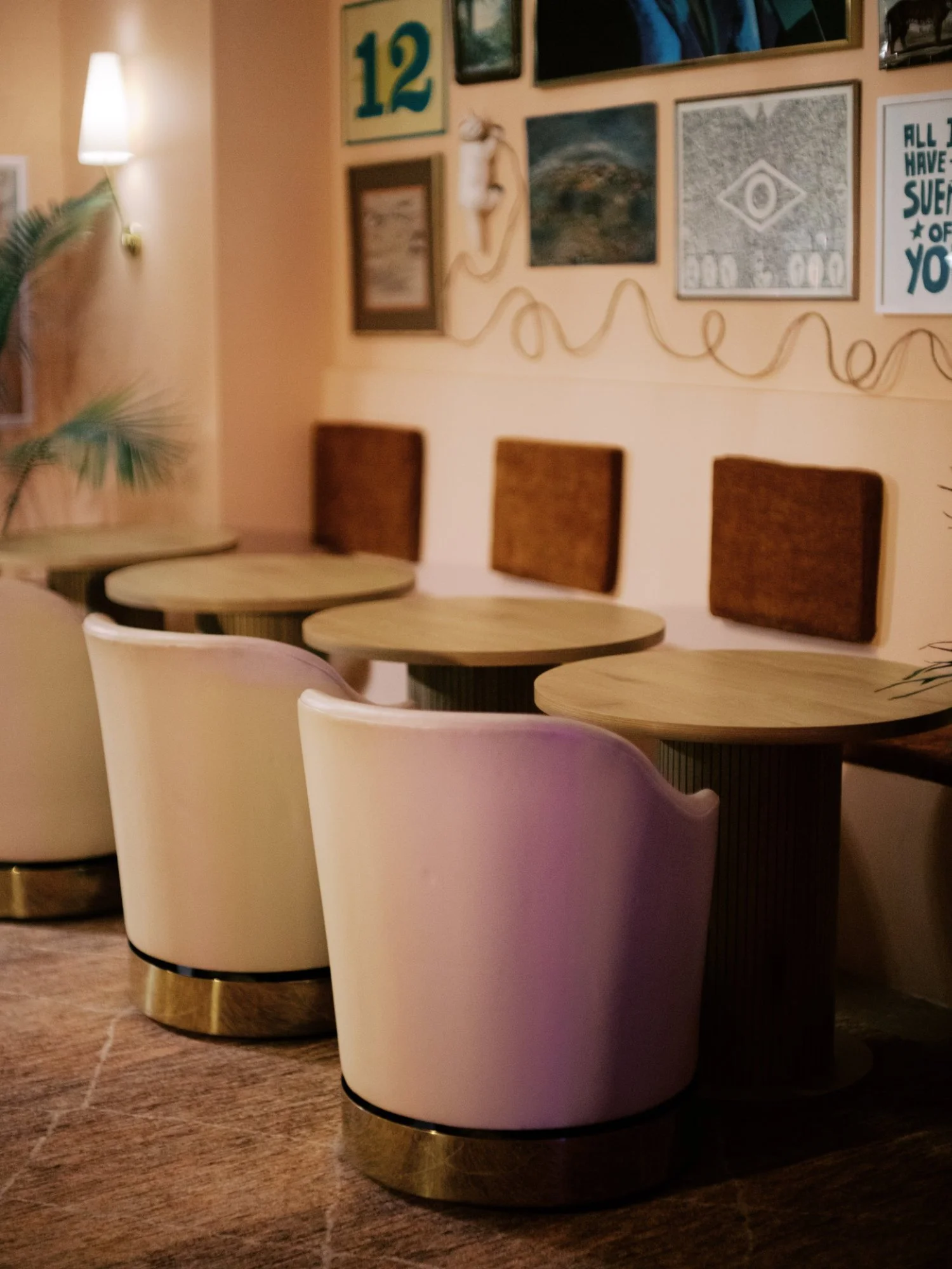 Empty tables and chairs in a cozy cafe or restaurant with a gallery wall of framed artwork and decor.