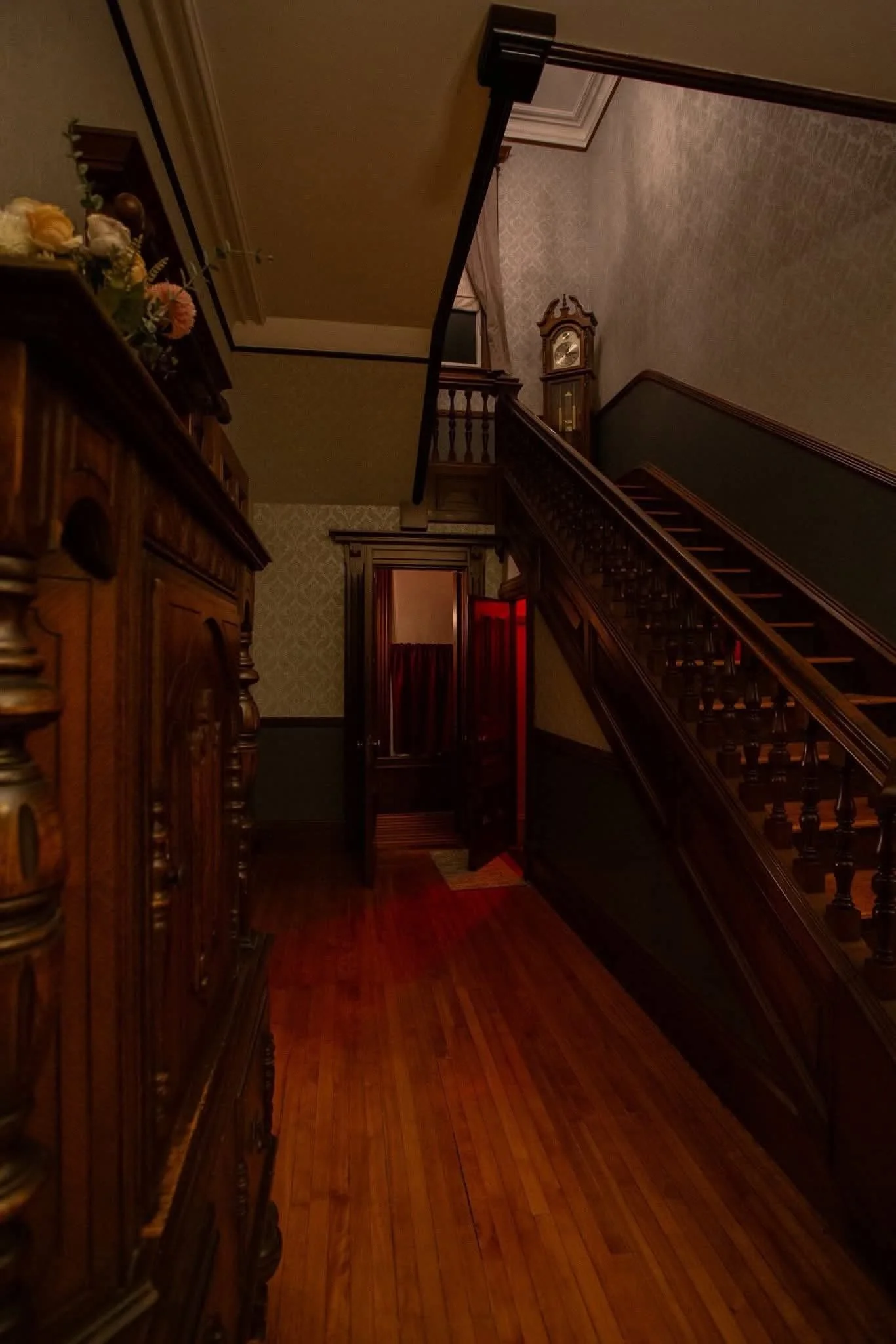 View of a staircase and hallway with vintage wooden decor and furniture in a dimly lit interior of the S.K. Pierce Mansion.