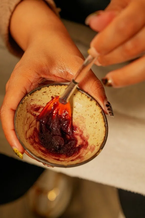 A person stirring a smoothie or milkshake with a spoon, in a glass with a dark red fruit or berry topping or mix-in.
