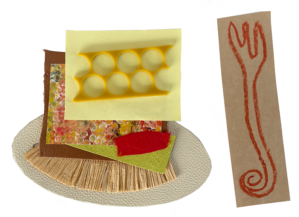 Mixed craft materials arranged on a white textured oval base, including patterned paper, colored tissue paper, felt, a yellow plastic object with six circular holes, and a piece of brown cardboard with a red crayon drawing of a fork.