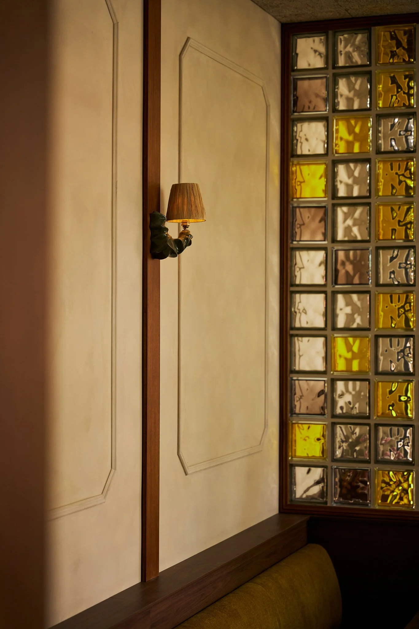 Interior view of a wall with a small wall-mounted lamp next to a glass block window with yellow and clear glass panes.