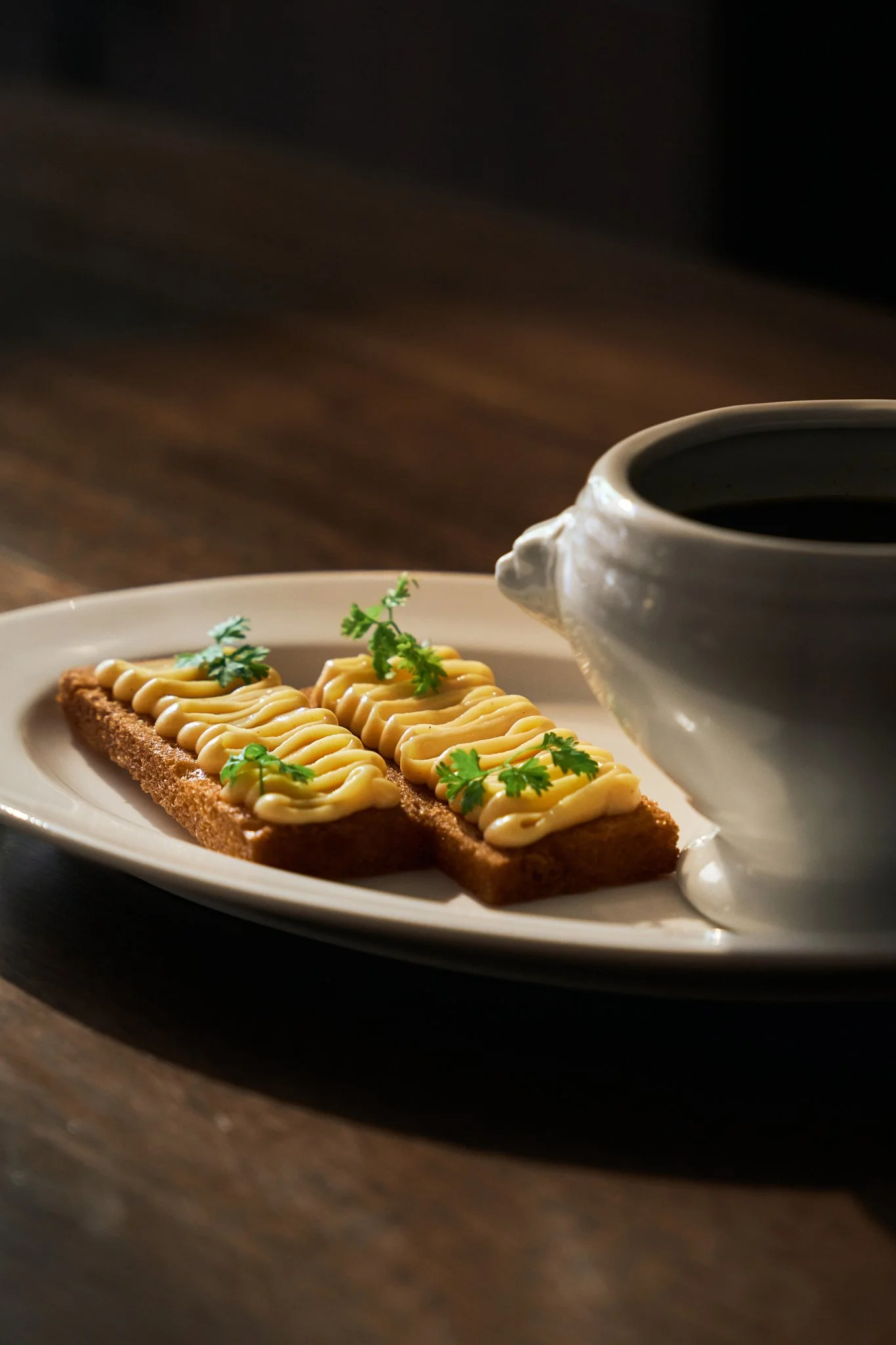 Two pieces of toast topped with mayonnaise and garnished with cilantro, accompanied by a cup of black coffee on a white plate.