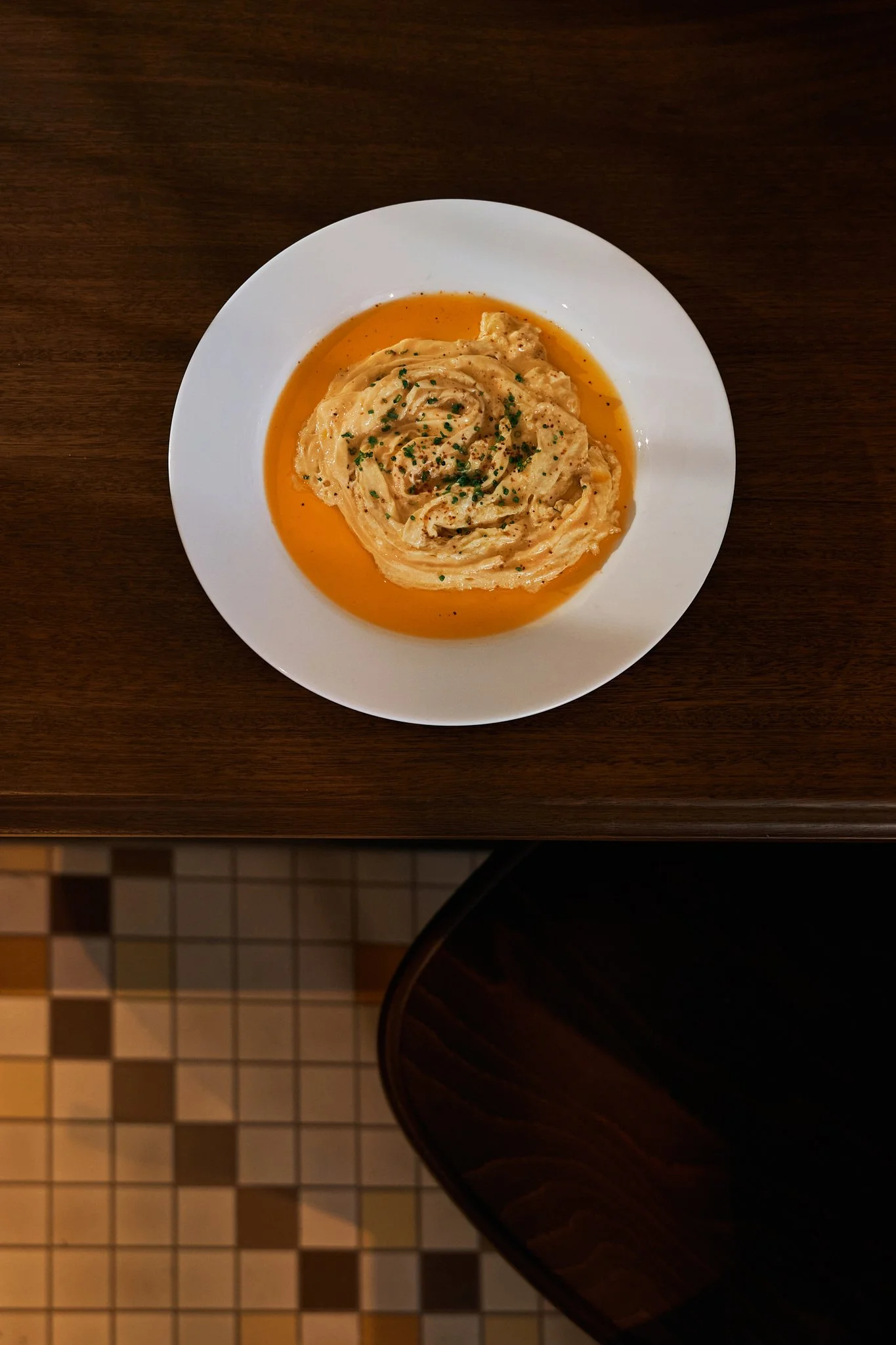 Plate of mashed potatoes with gravy garnished with chopped chives, on a wooden table.