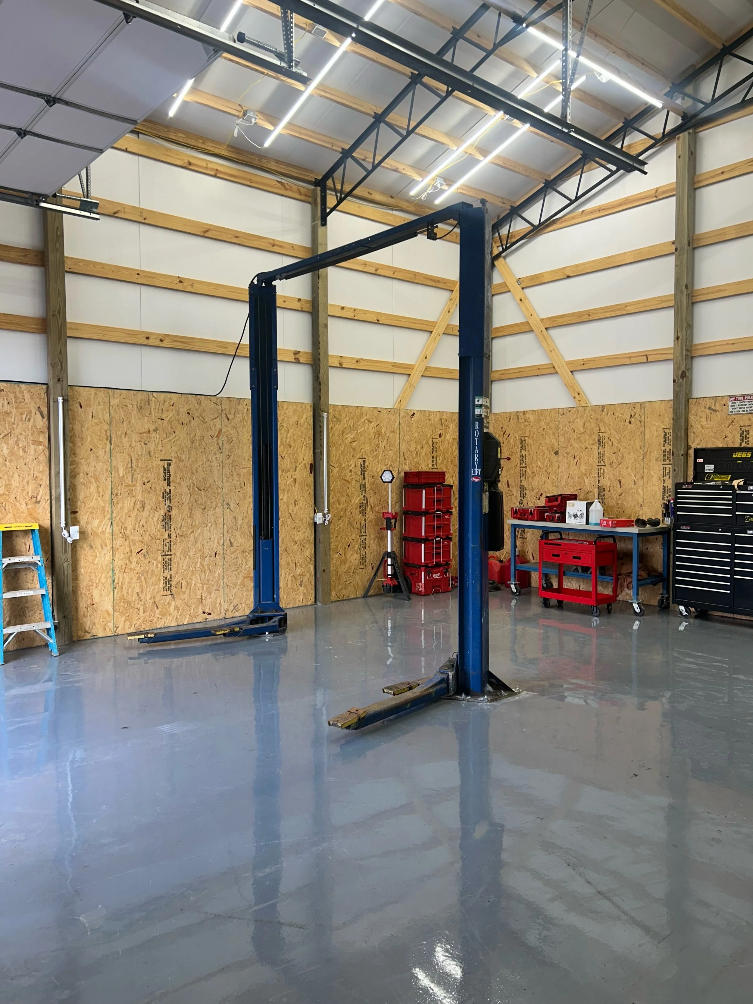 Garage workshop with a vehicle lift, workbench, and storage tools in a new, unfinished space.