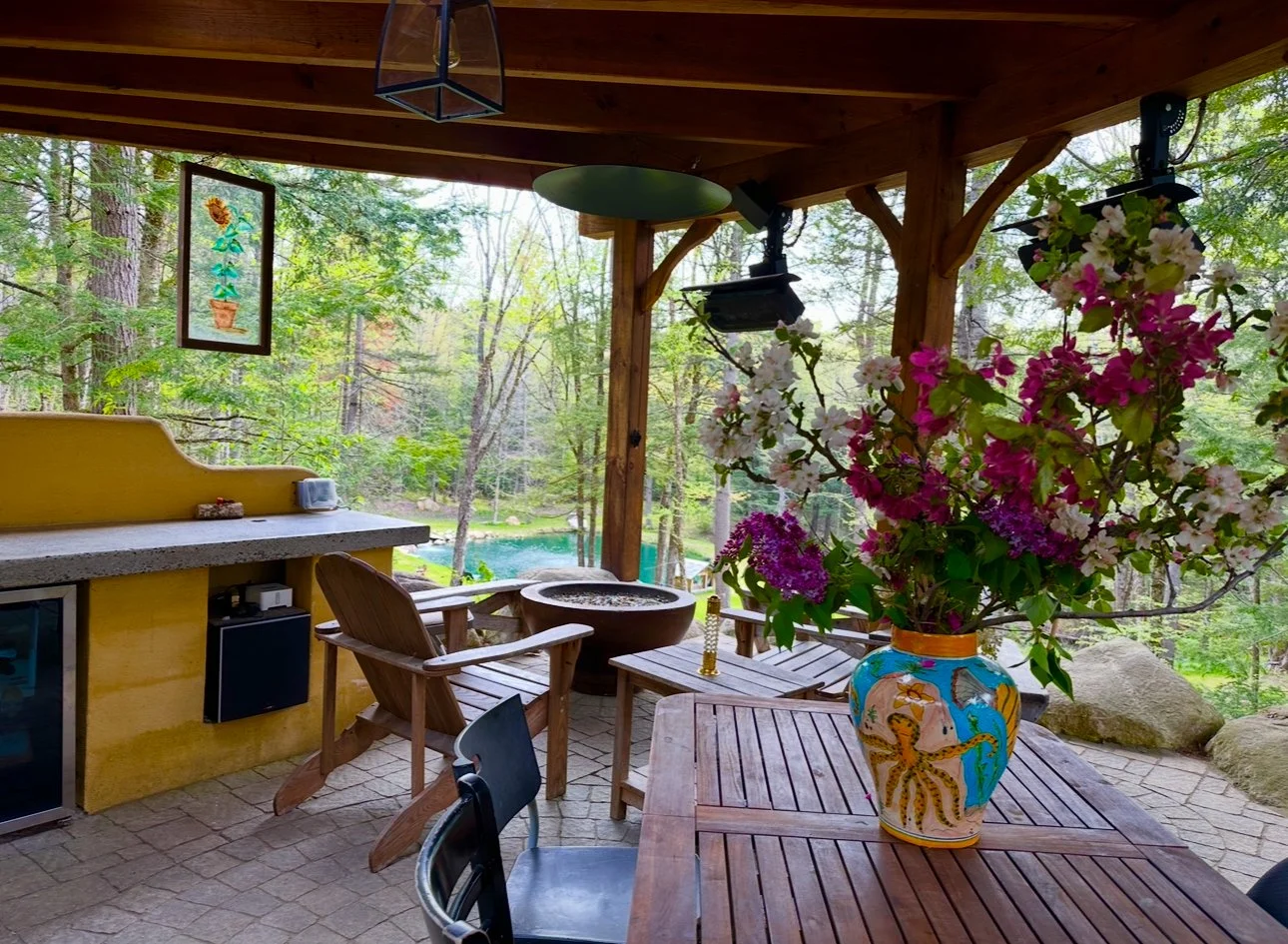 Daytime pic of outdoor kitchen, custom built acid stained cement gas fireplace with colored glass.