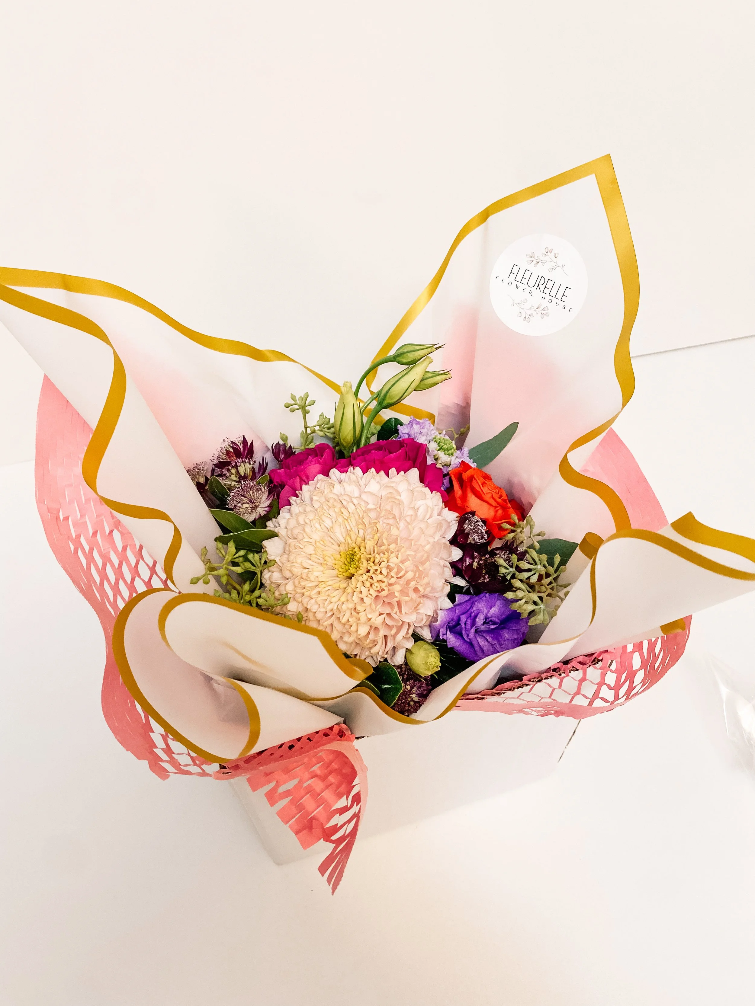 Colorful bouquet of assorted flowers wrapped in pink and white paper with gold trim.
