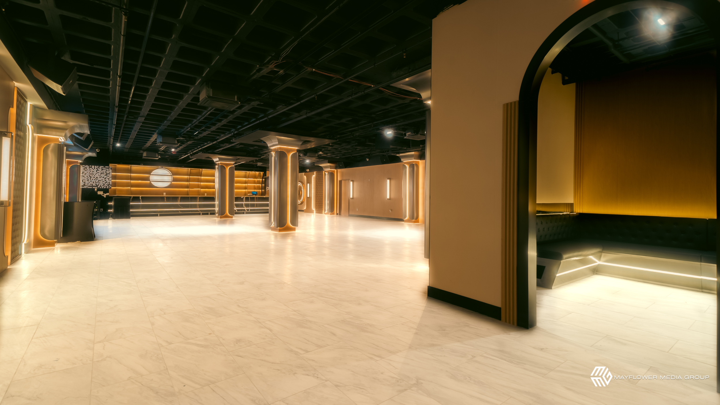 An empty modern lobby with black ceiling, gold accents, light-colored tiled floor, and a reception desk with a digital screen in the background.