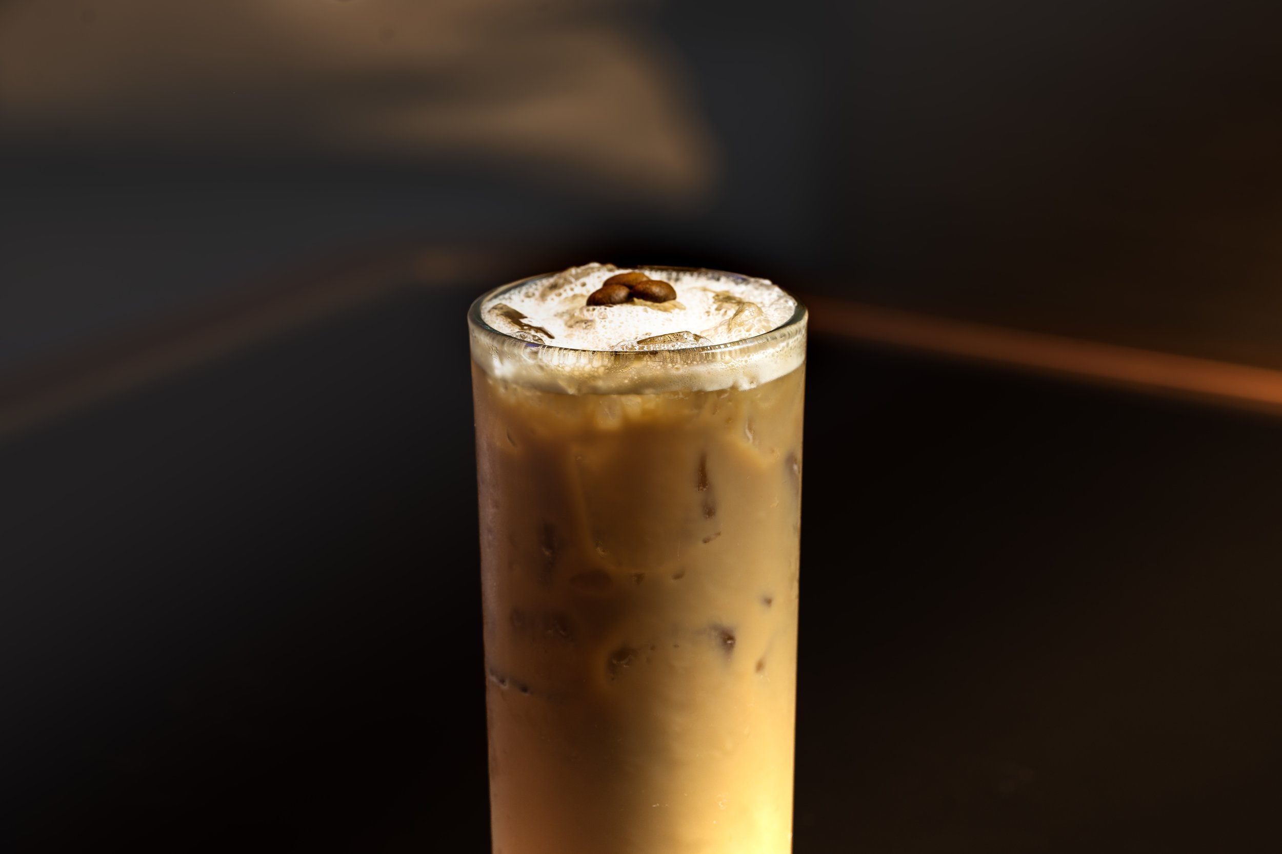 A tall glass of iced coffee topped with whipped cream and coffee beans on top.