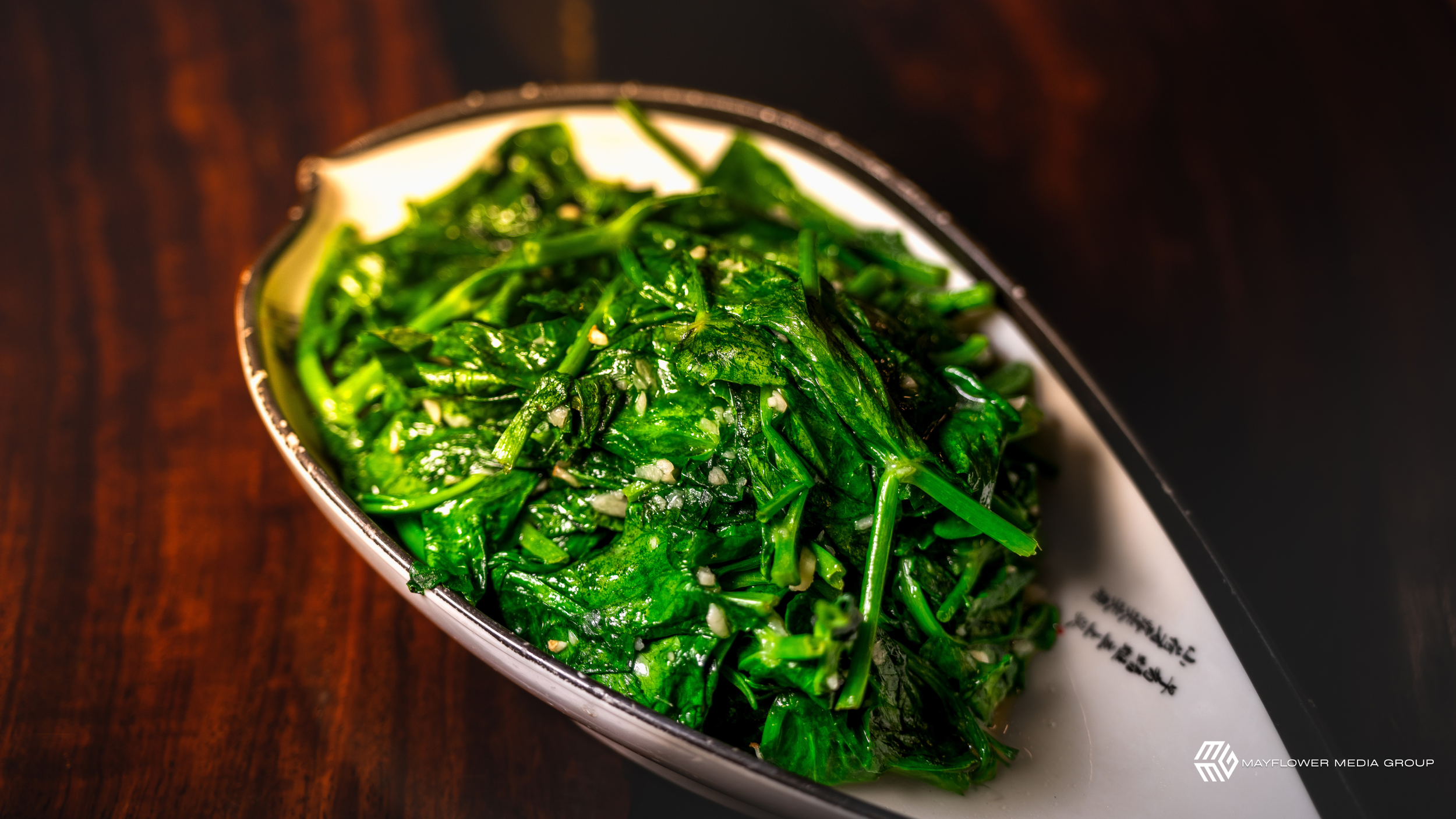 A close-up of a dish with cooked leafy greens, possibly spinach, served in a black and white dish on a wooden surface.