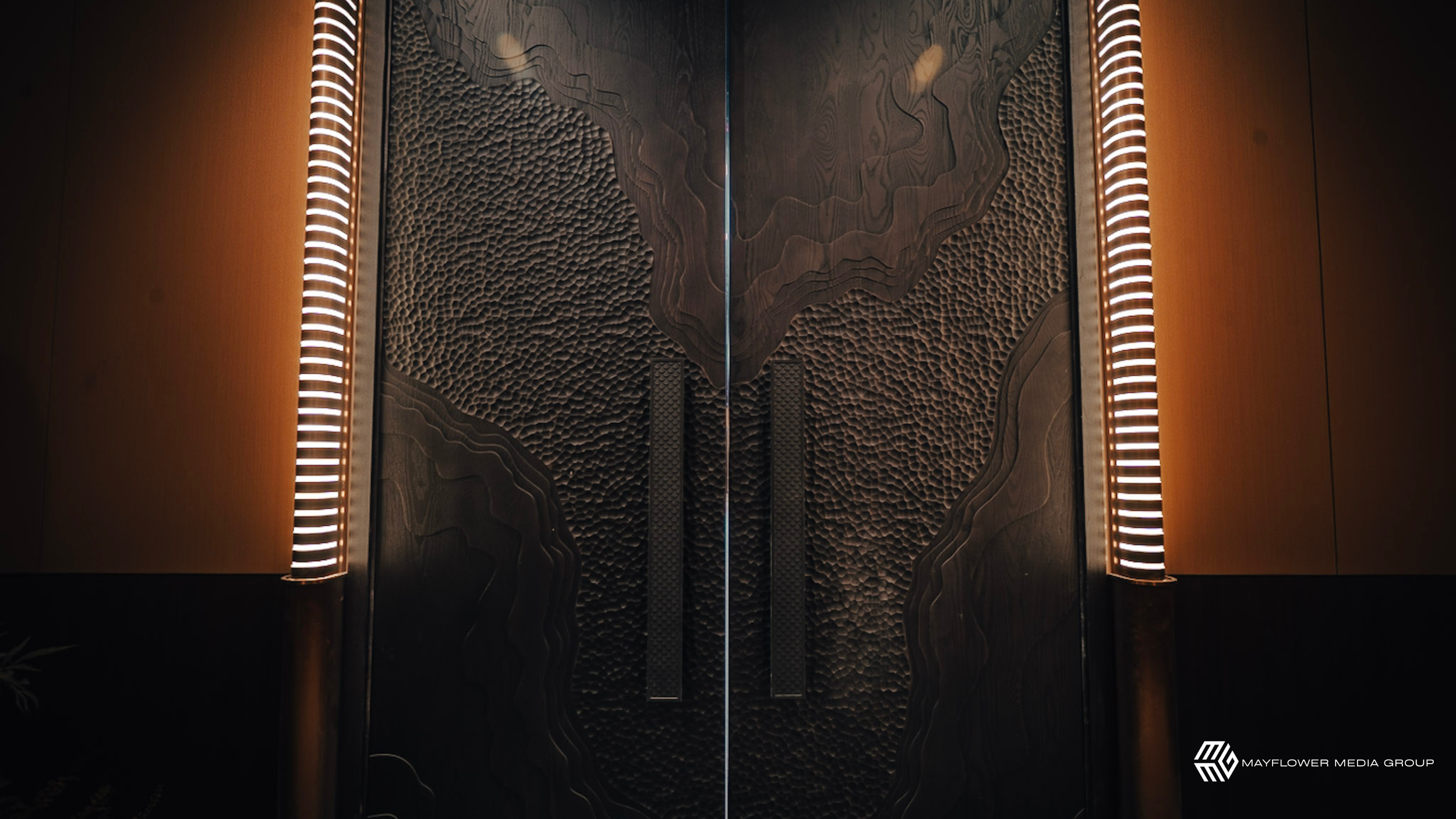 Elevator doors with a textured wood design and illuminated trim on the sides.