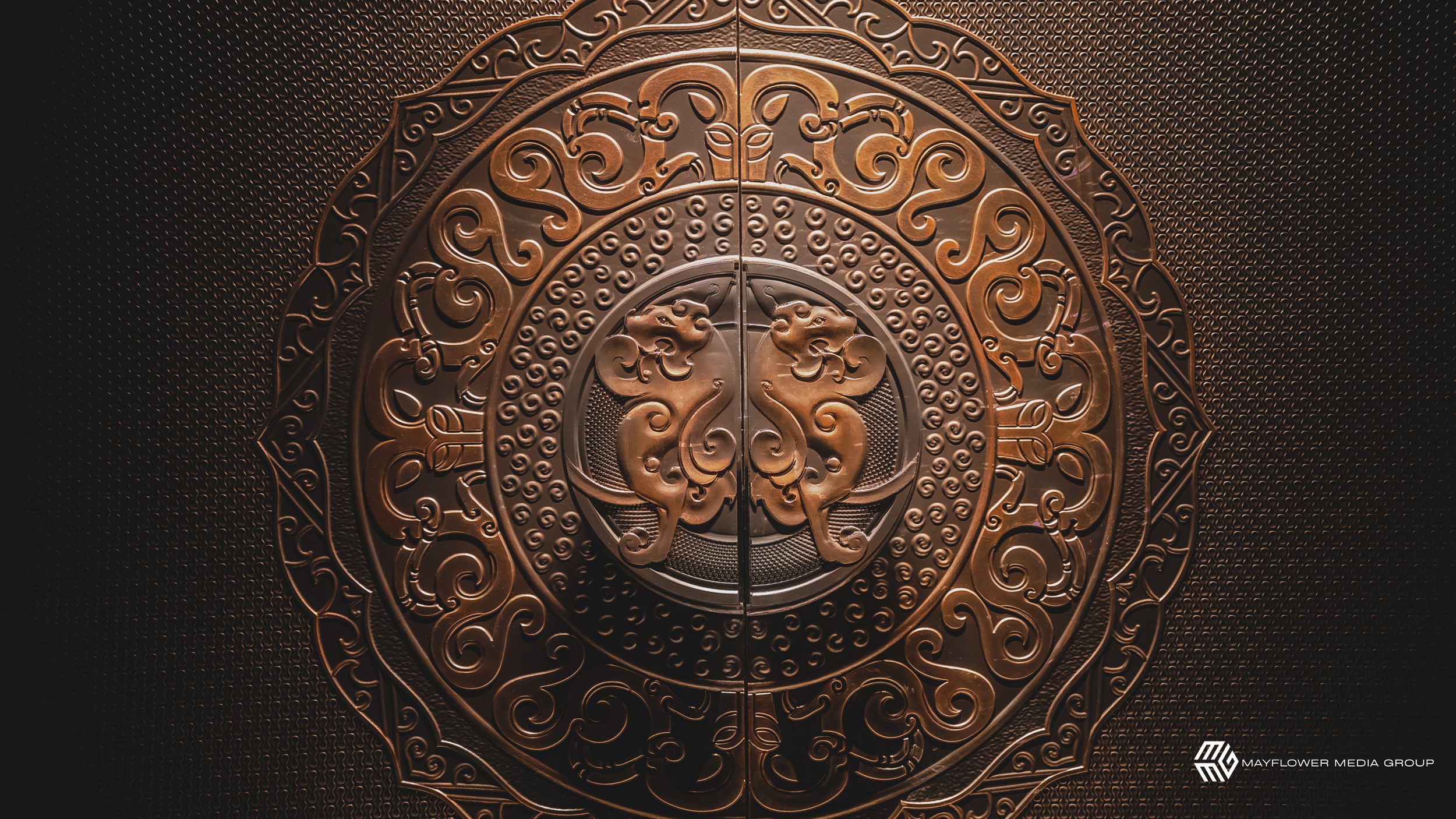 A decorative bronze door with intricate swirling patterns and two lion heads facing each other in the center.