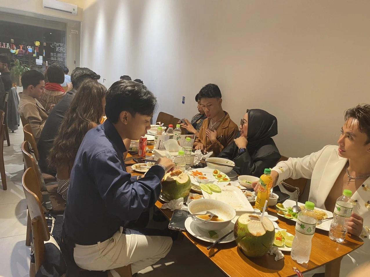 Group of people dining at a restaurant, with food, drinks, and coconuts on the table.