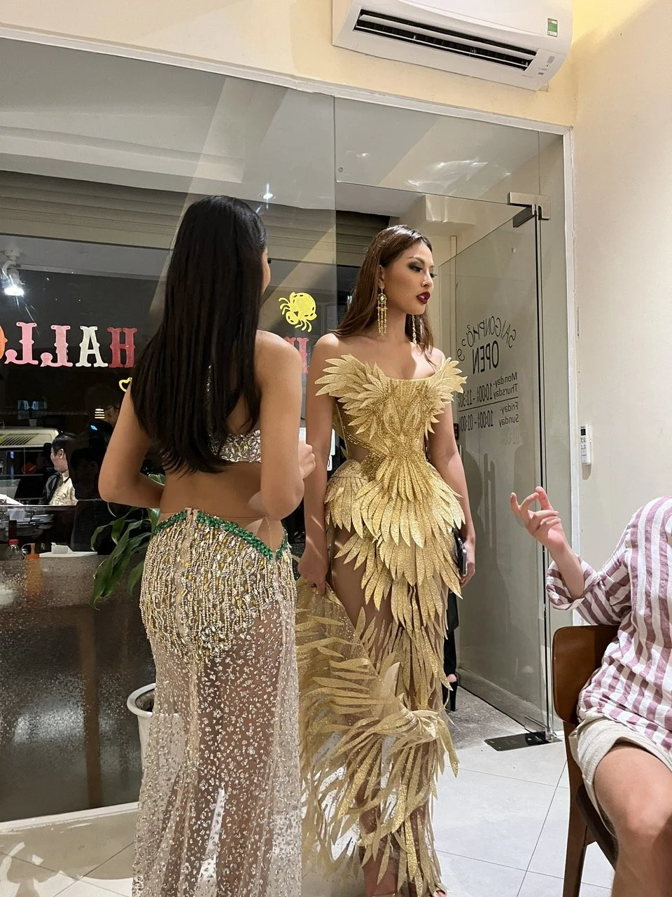 Two women in glamorous outfits having a conversation inside a restaurant or cafe.