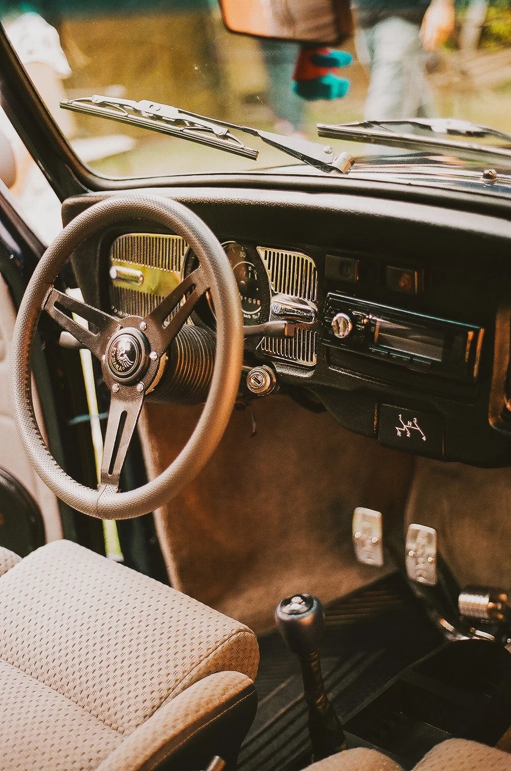 Interior of a vintage Volkswagen vehicle with a classic steering wheel, dashboard, manual gear shift, and cloth seats.