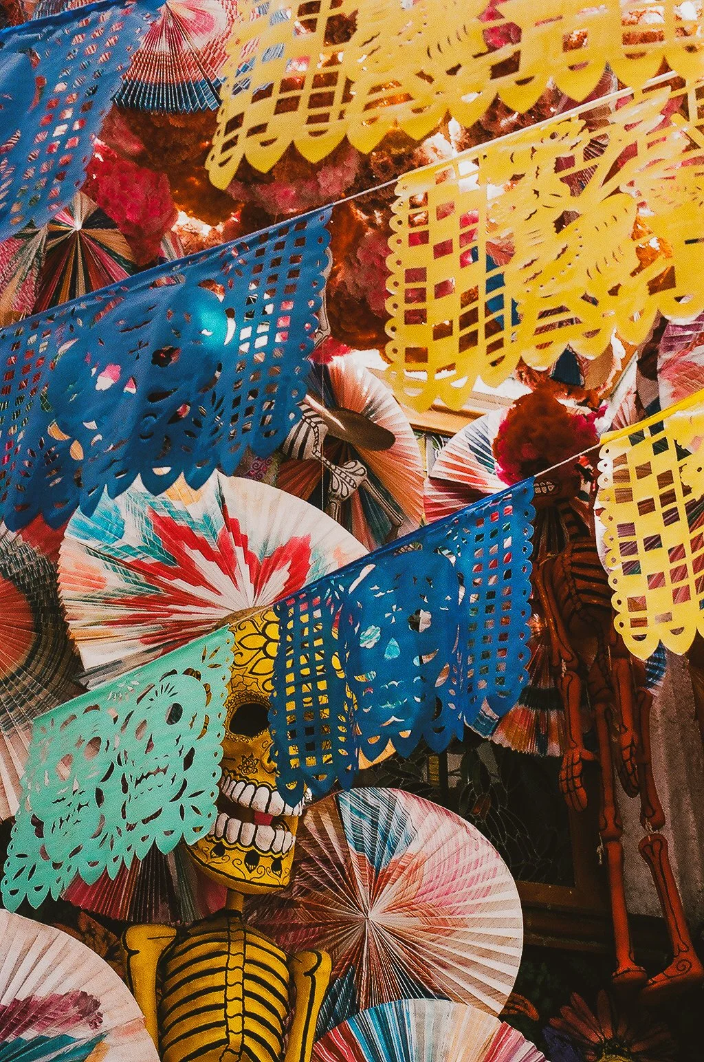 Colorful paper fans, papel picado banners, and a decorative skeleton figure, typical of Día de los Muertos decorations.