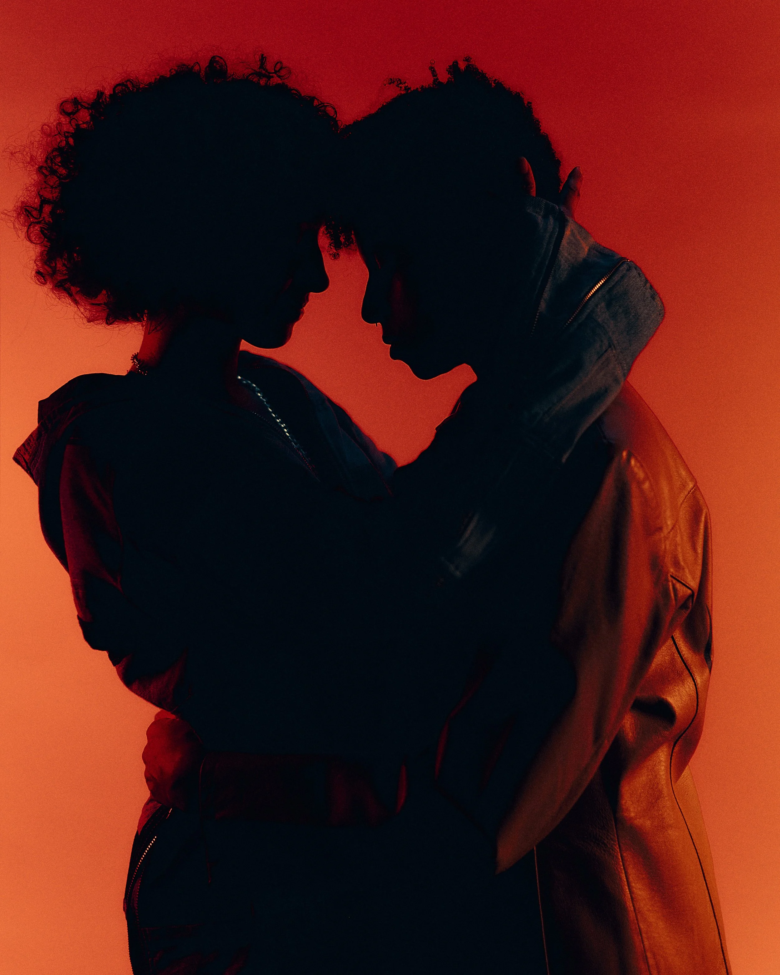 Silhouettes of a man and woman in an intimate pose, facing each other with foreheads touching, against a red background.