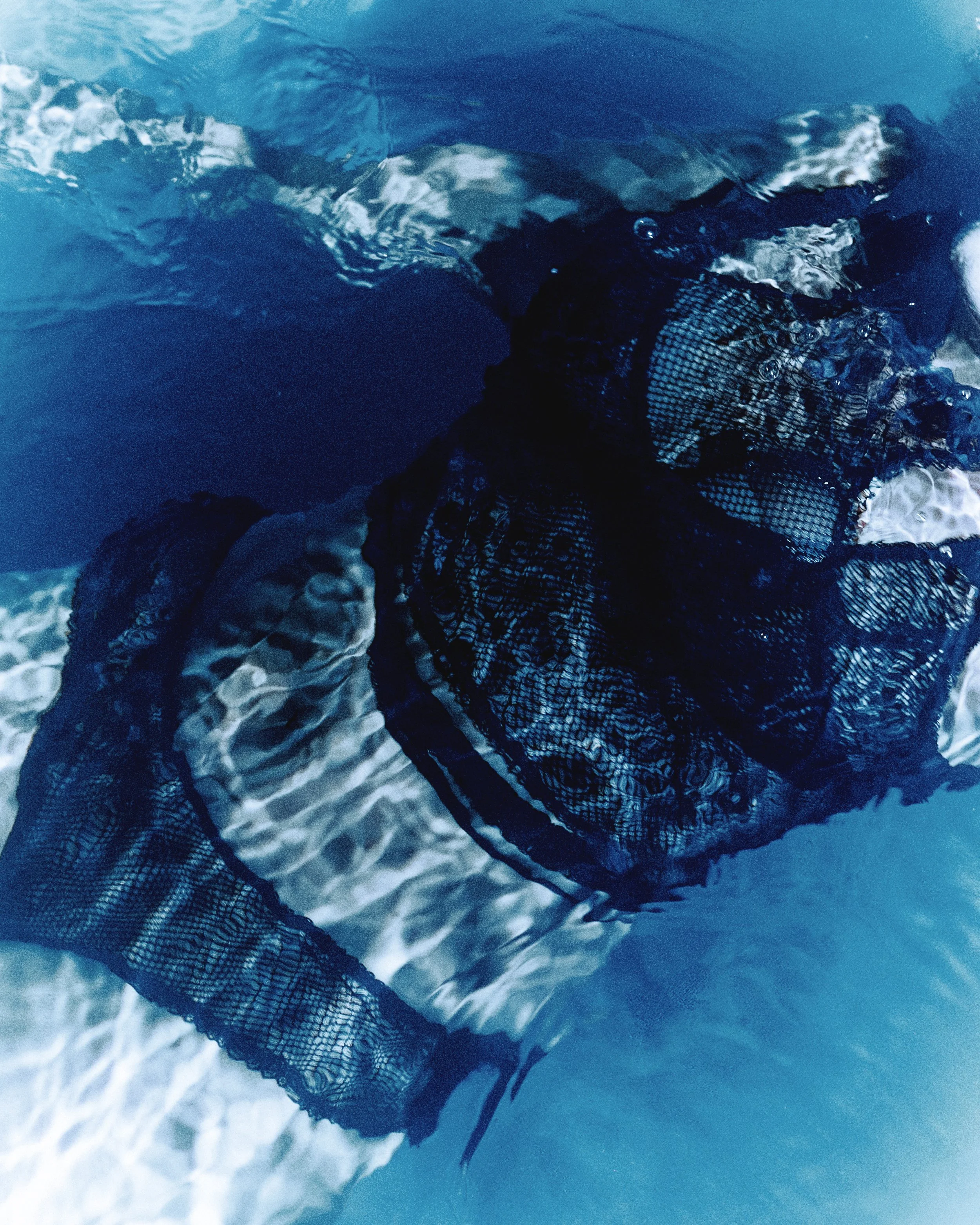 A dark, patterned fabric submerged in water with reflections and ripples.
