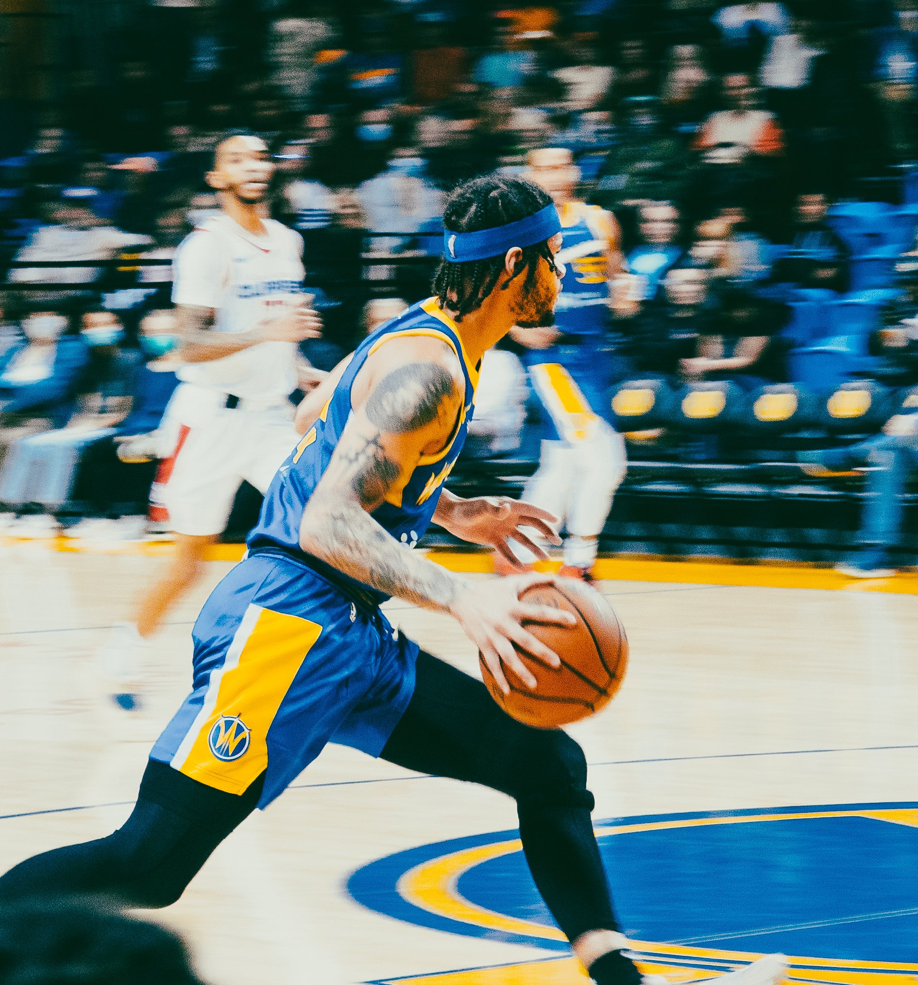 A basketball player in a blue and yellow uniform running with the ball during a game, with a crowd in the background.