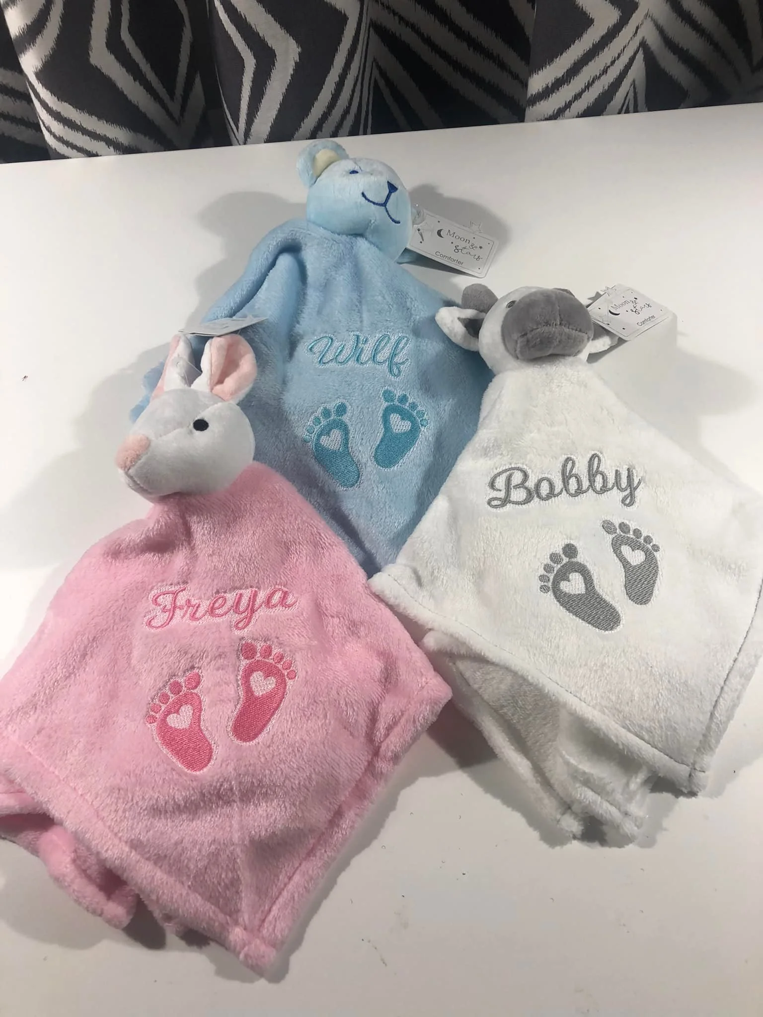 Set of three plush baby towels with embroidered names, animal faces, and paw prints on a white surface.