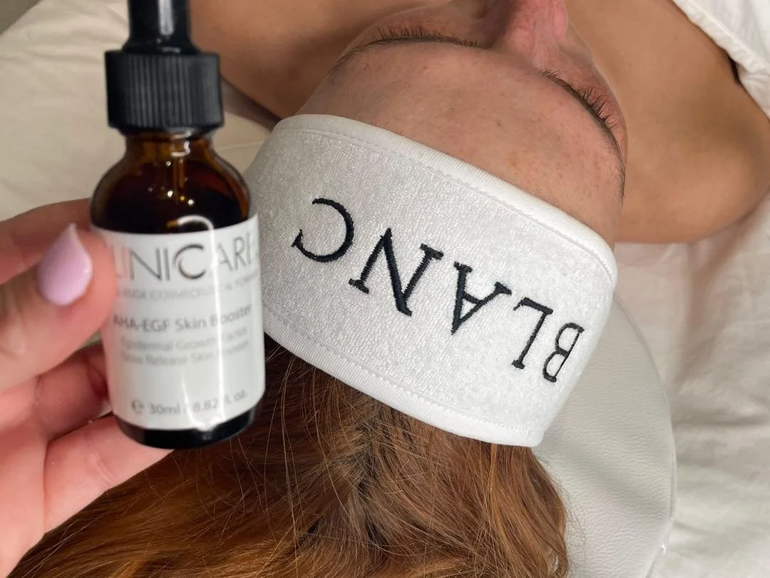 A person lying down with a white headband reading 'BLANC' covering their forehead, holding a small bottle of skincare serum labeled 'PRO VEGF'.